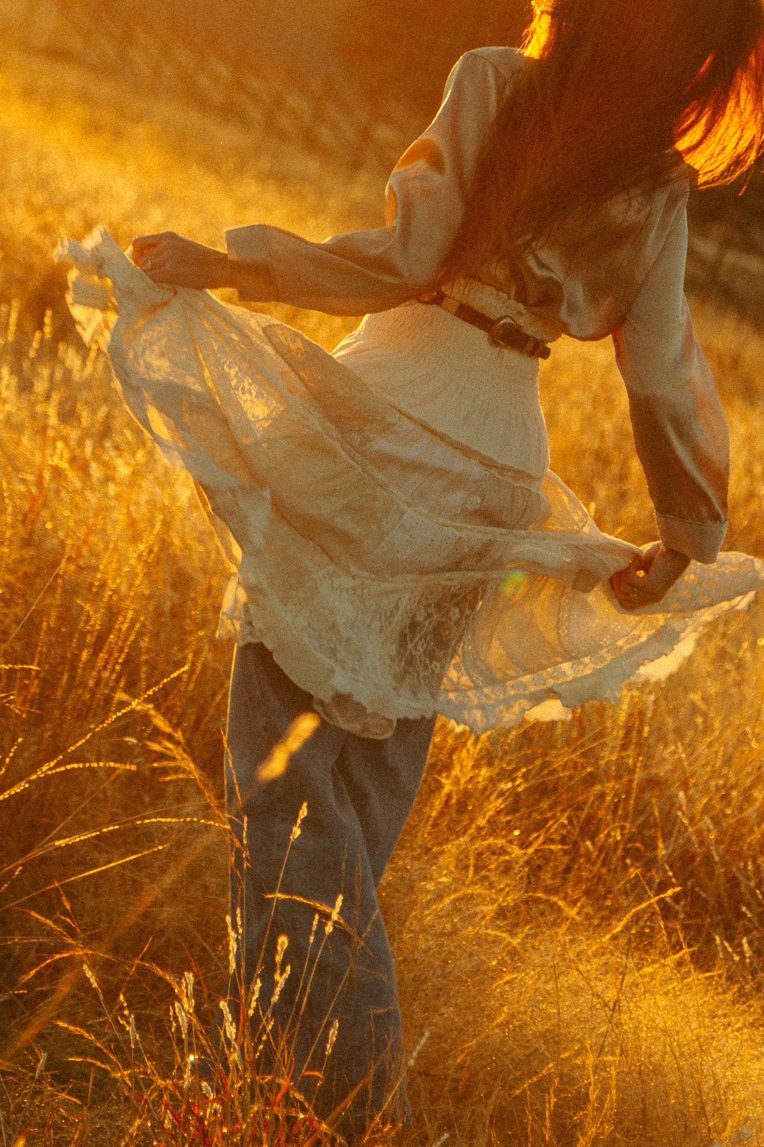 Dancing fabric of white dress catches golden light in autumn field.