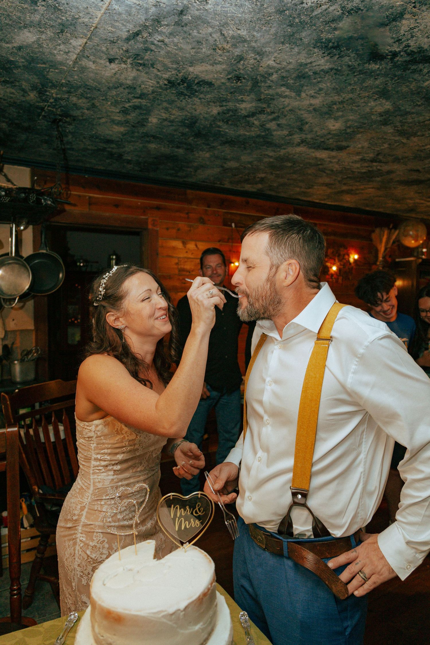 Newly married couple share bites of cake at indoor reception.