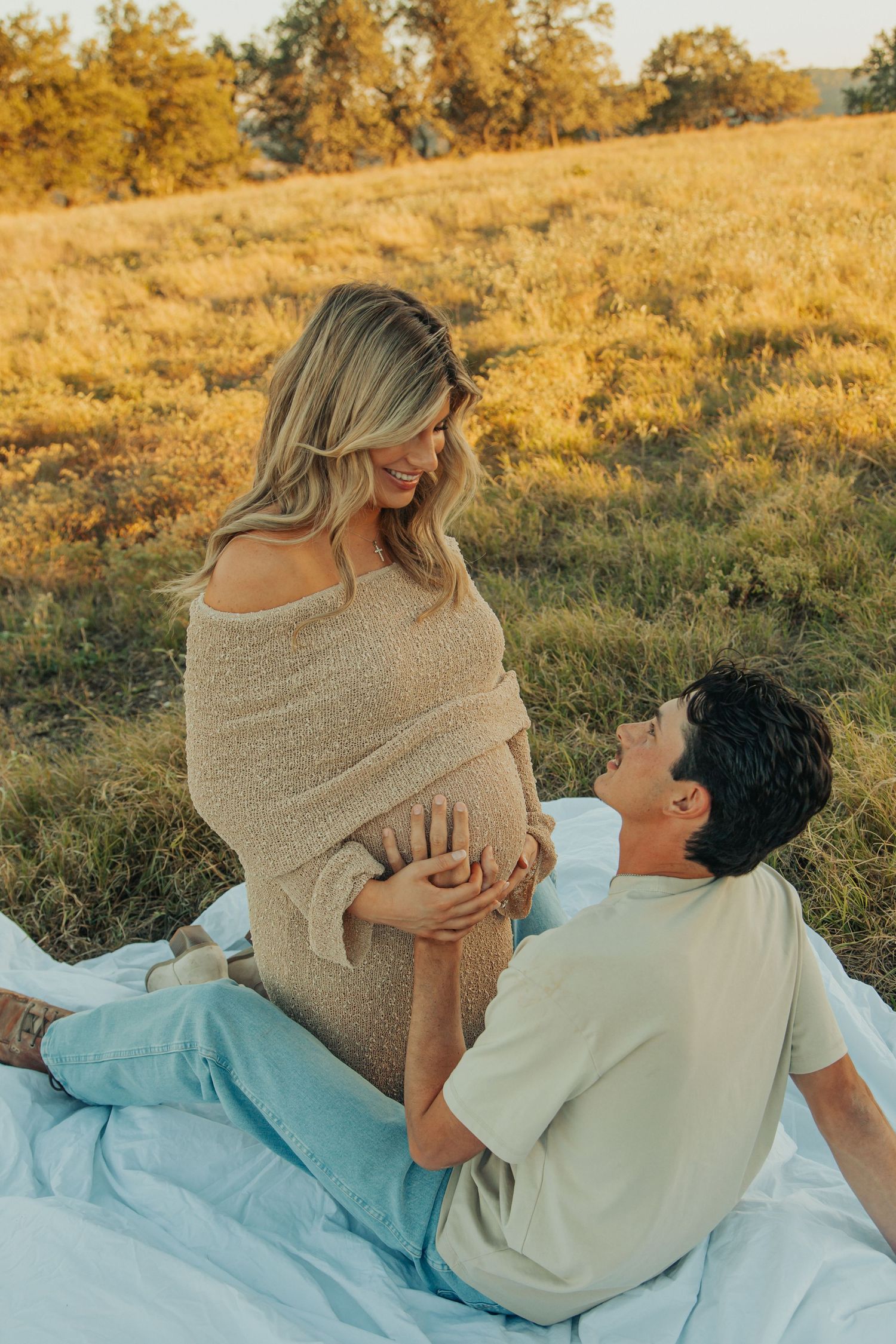 Intimate maternity photo of a couple on a blanket in a sun-drenched field during golden hour.
