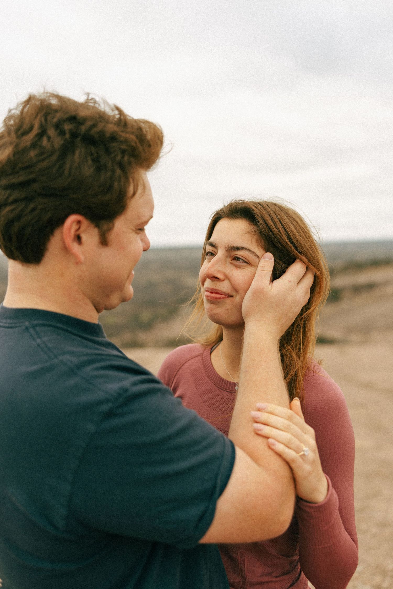 A tender moment between a couple on a desert cliff with soft natural lighting.