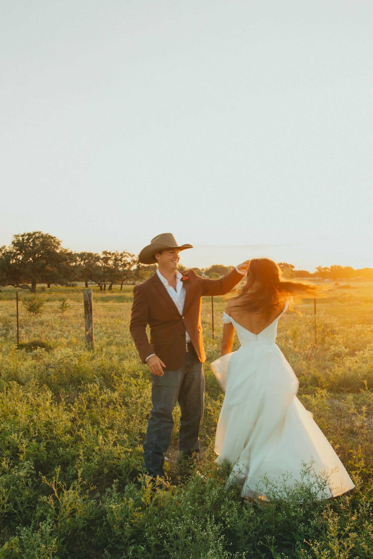 A couple shares a playful moment during their sunset wedding photoshoot in a Texas field.
