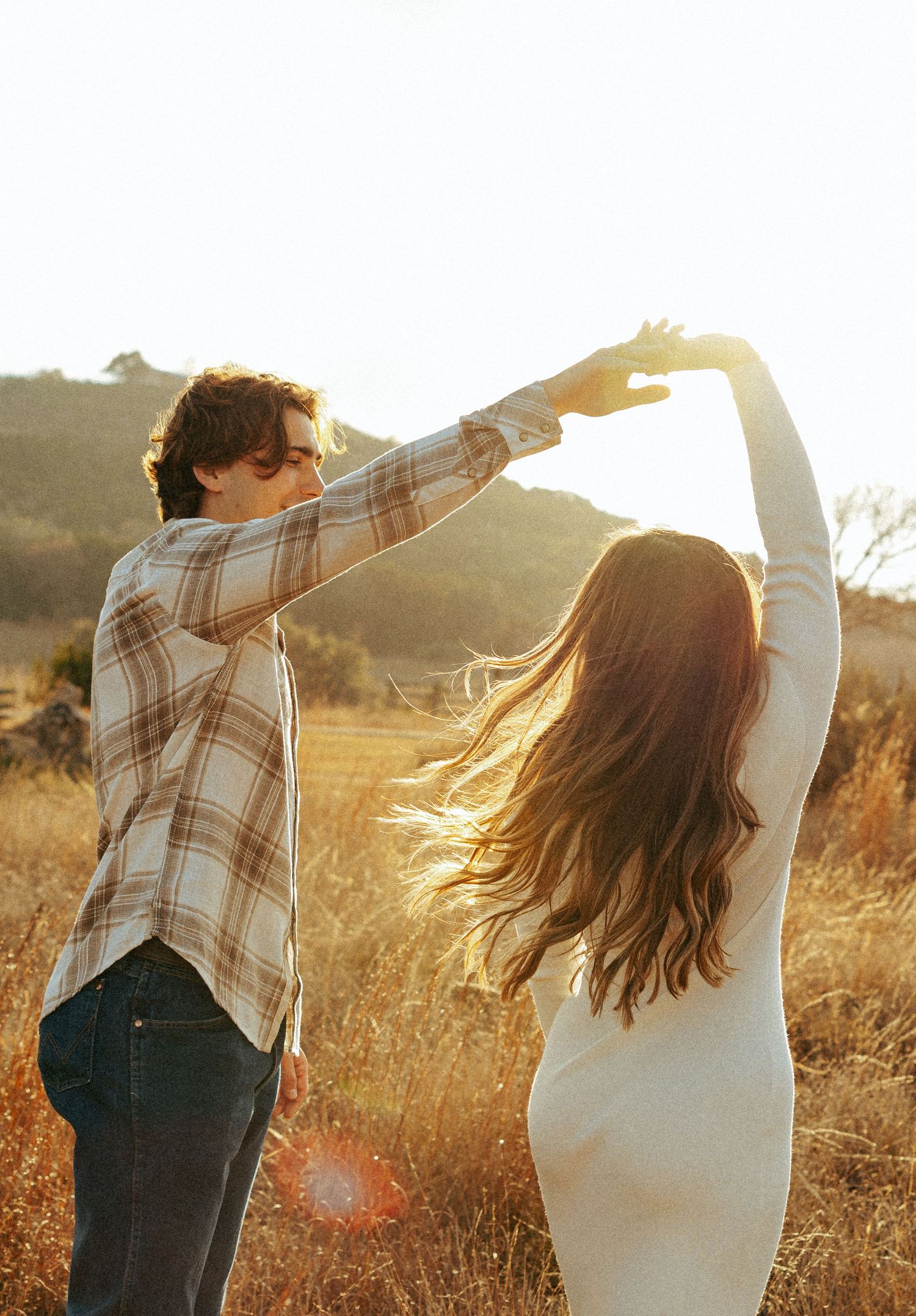 Dancing couple silhouetted against warm sunlight in a rustic field setting.