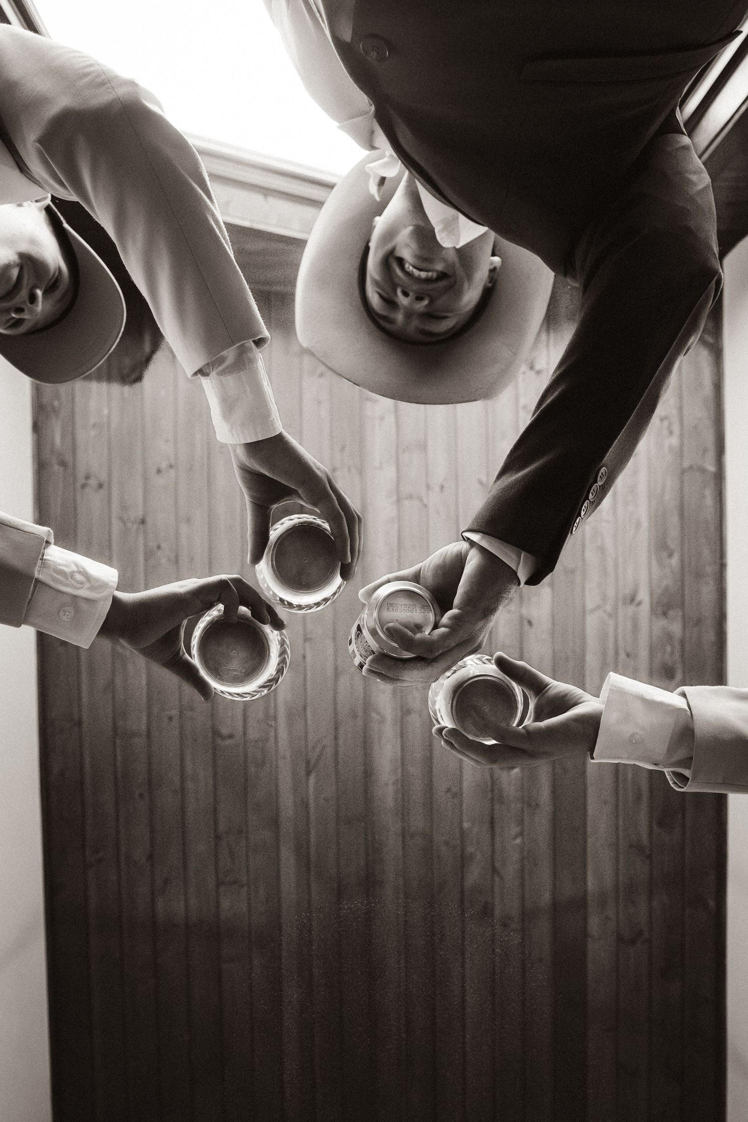 Overhead view of groomsmen in cowboy hats toasting with drinks in black and white.