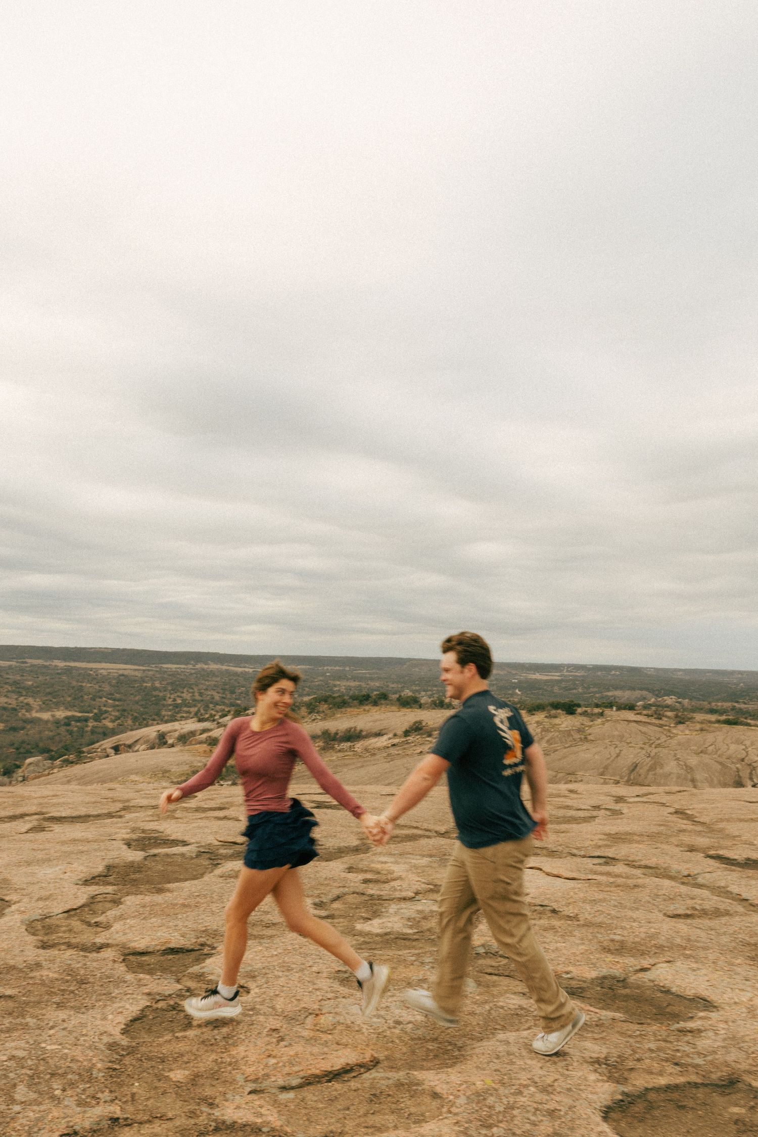 A joyful couple dancing together on a desert cliff with an overcast sky.