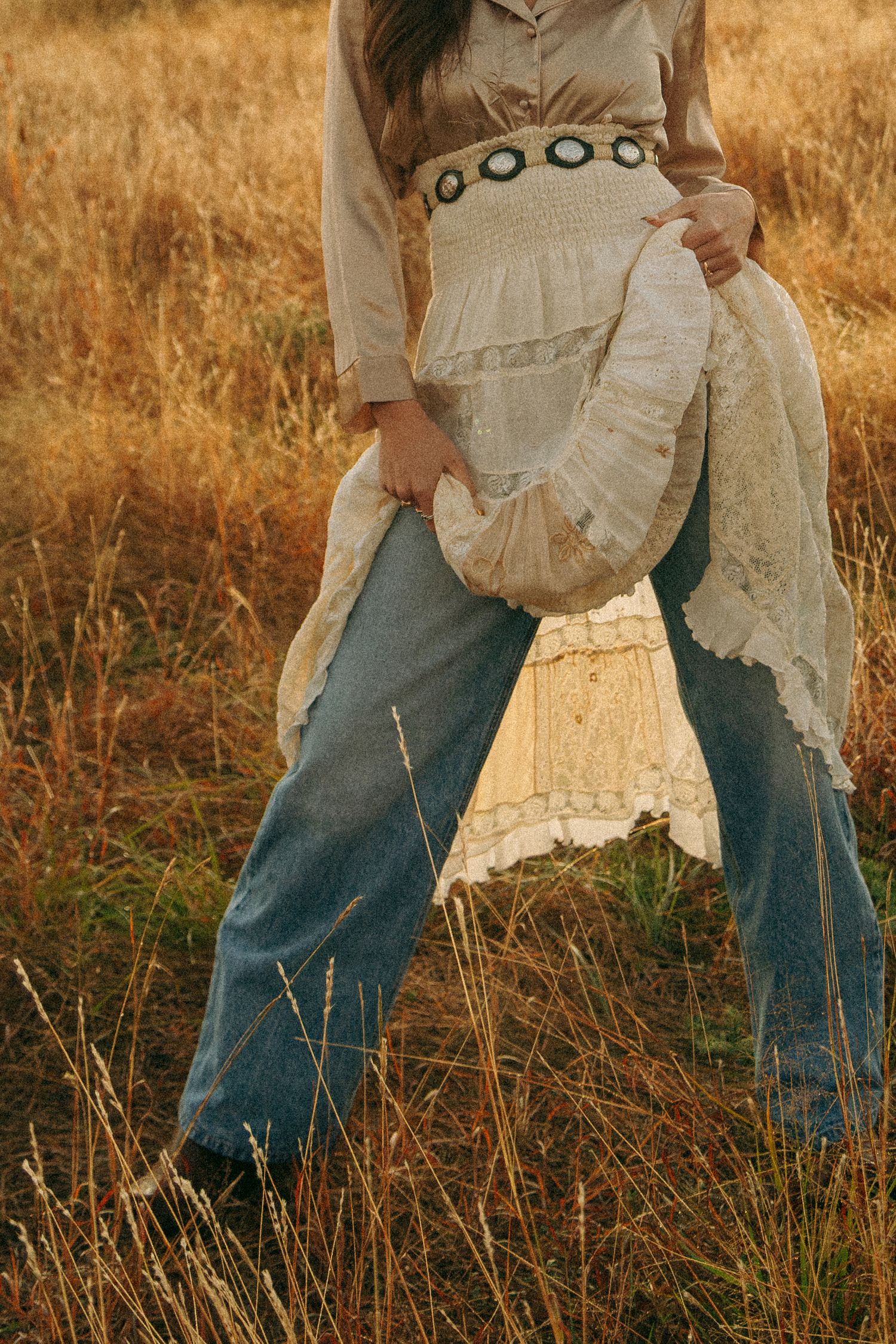 Close-up details of vintage-style white skirt and blue jeans in tall grass.
