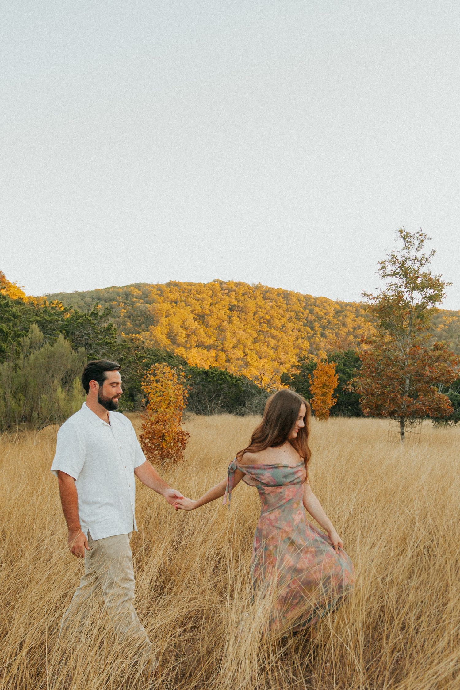 Couple dancing playfully through a golden field at sunset.