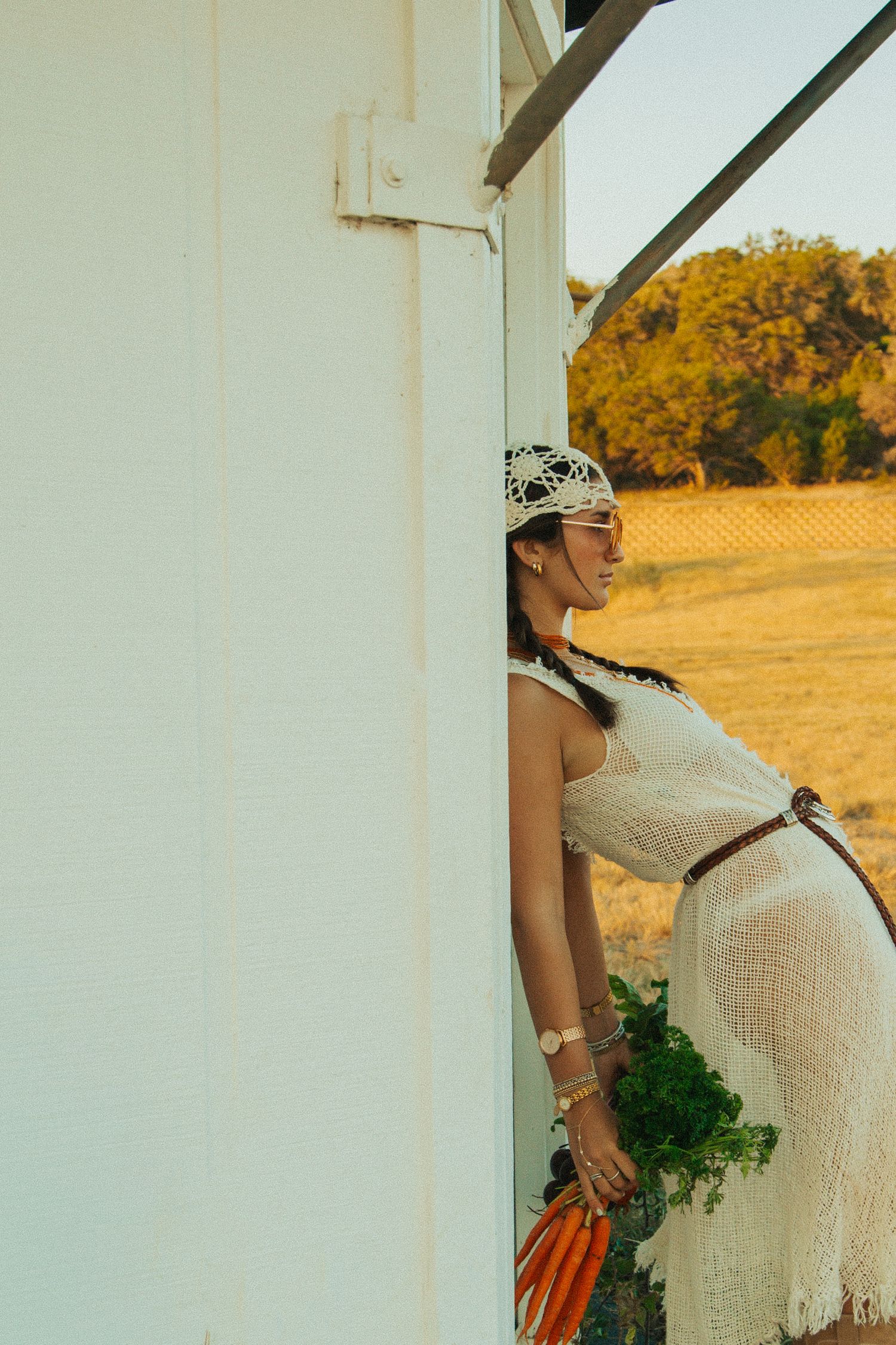 A woman in a white dress contrasts against golden field and building in artistic outdoor portrait.