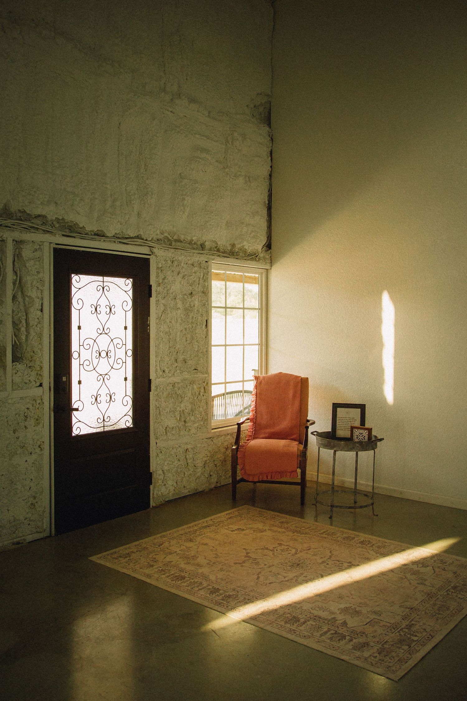 Empty room with white walls, orange chair, and dramatic sunlight streaming through ornate door windows.