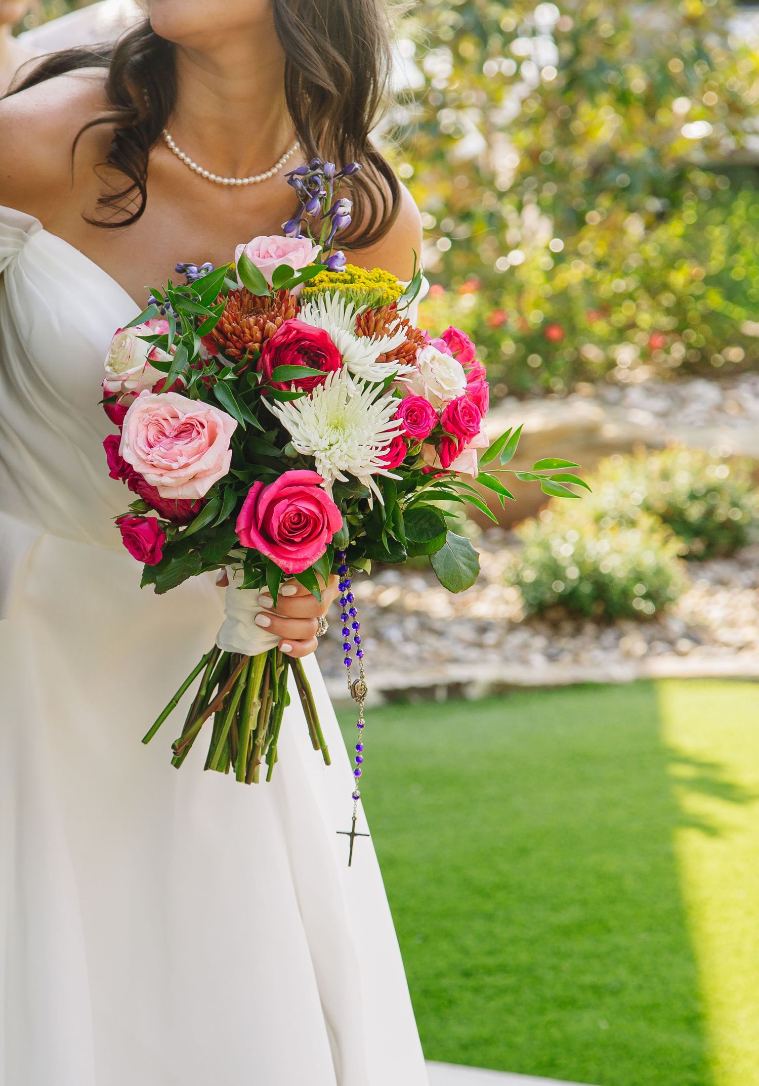 Vibrant pink and white bridal bouquet with roses and greenery against a garden background.