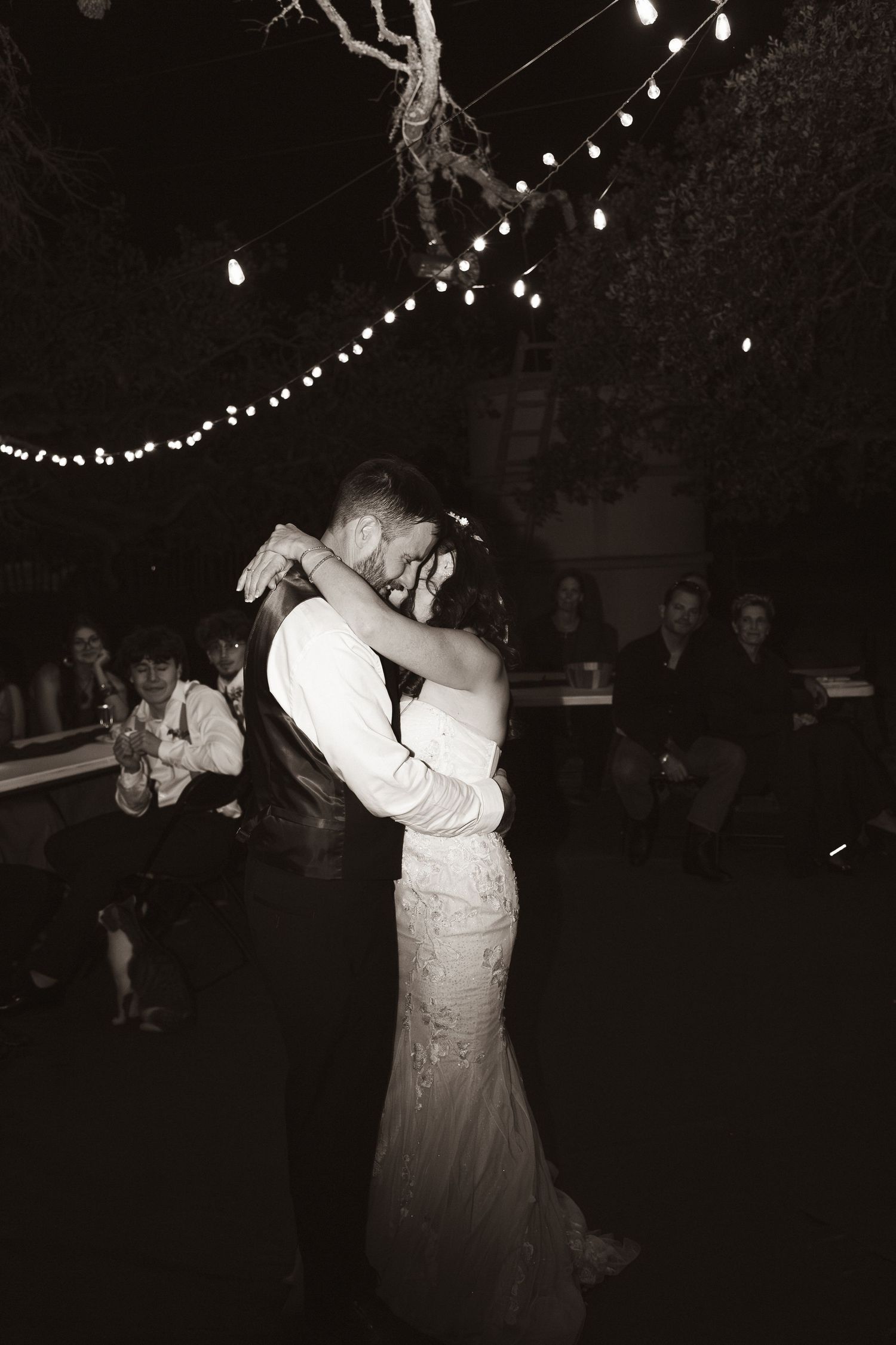 Newly married couple dancing under string lights at outdoor reception.