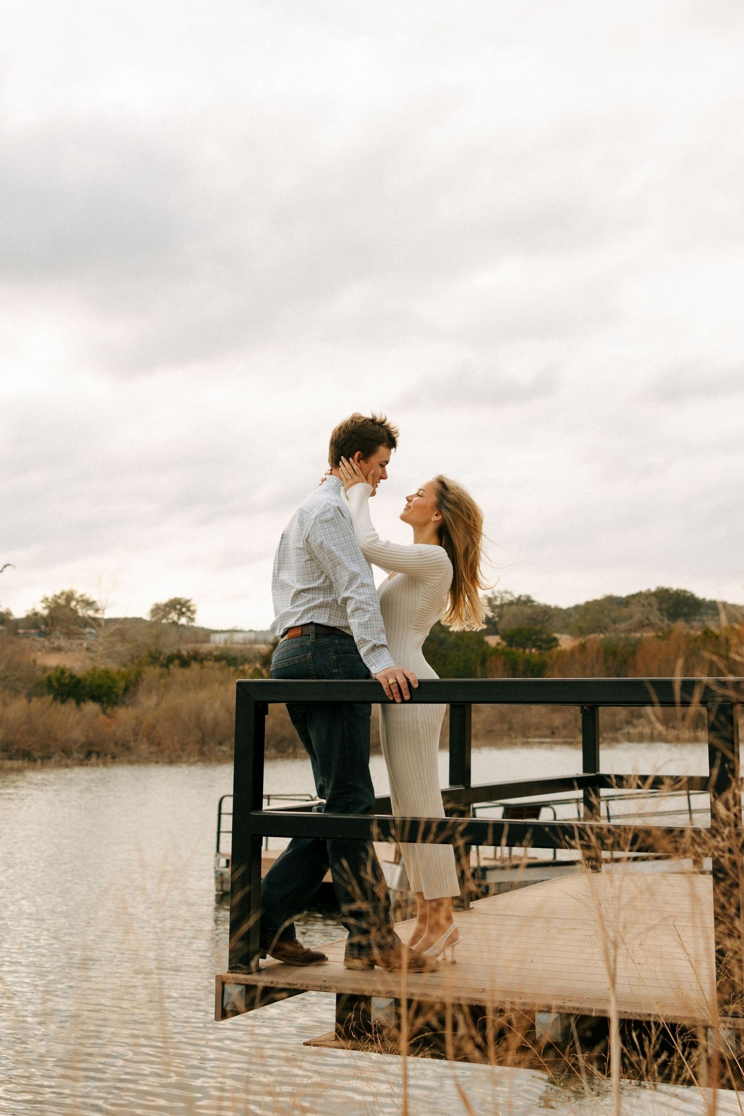 Romantic moment captured on lakeside dock with cloudy sky and water reflections.