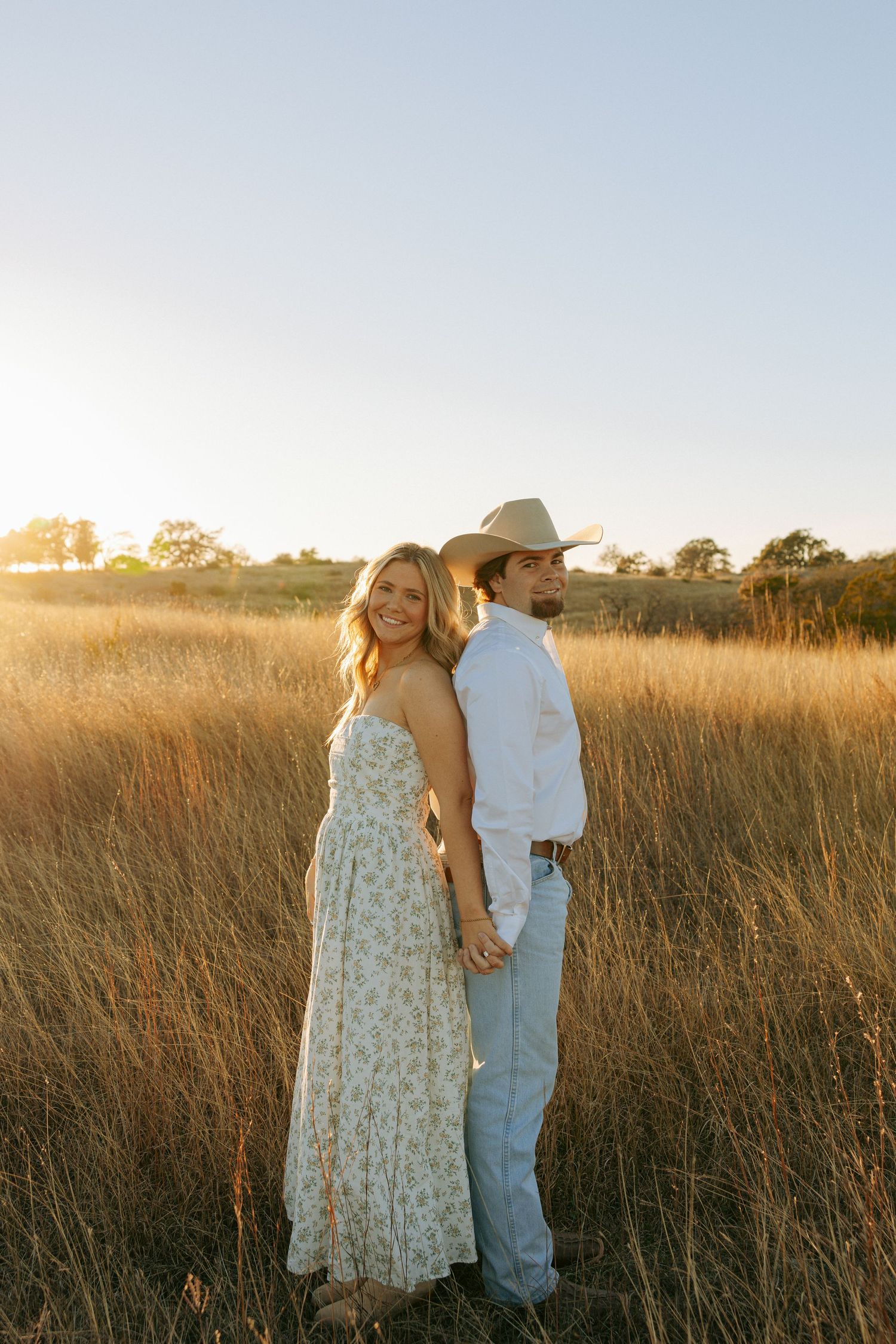 Couple posing in a sun-drenched field of tall grass at sunset.