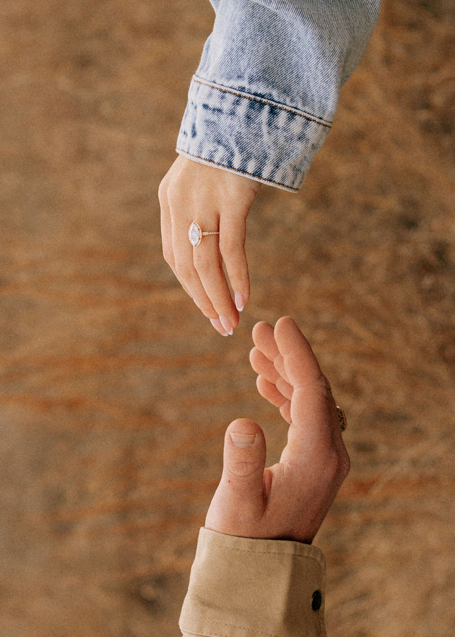 Close-up shot of a newly engaged couple reaching for each others hand.