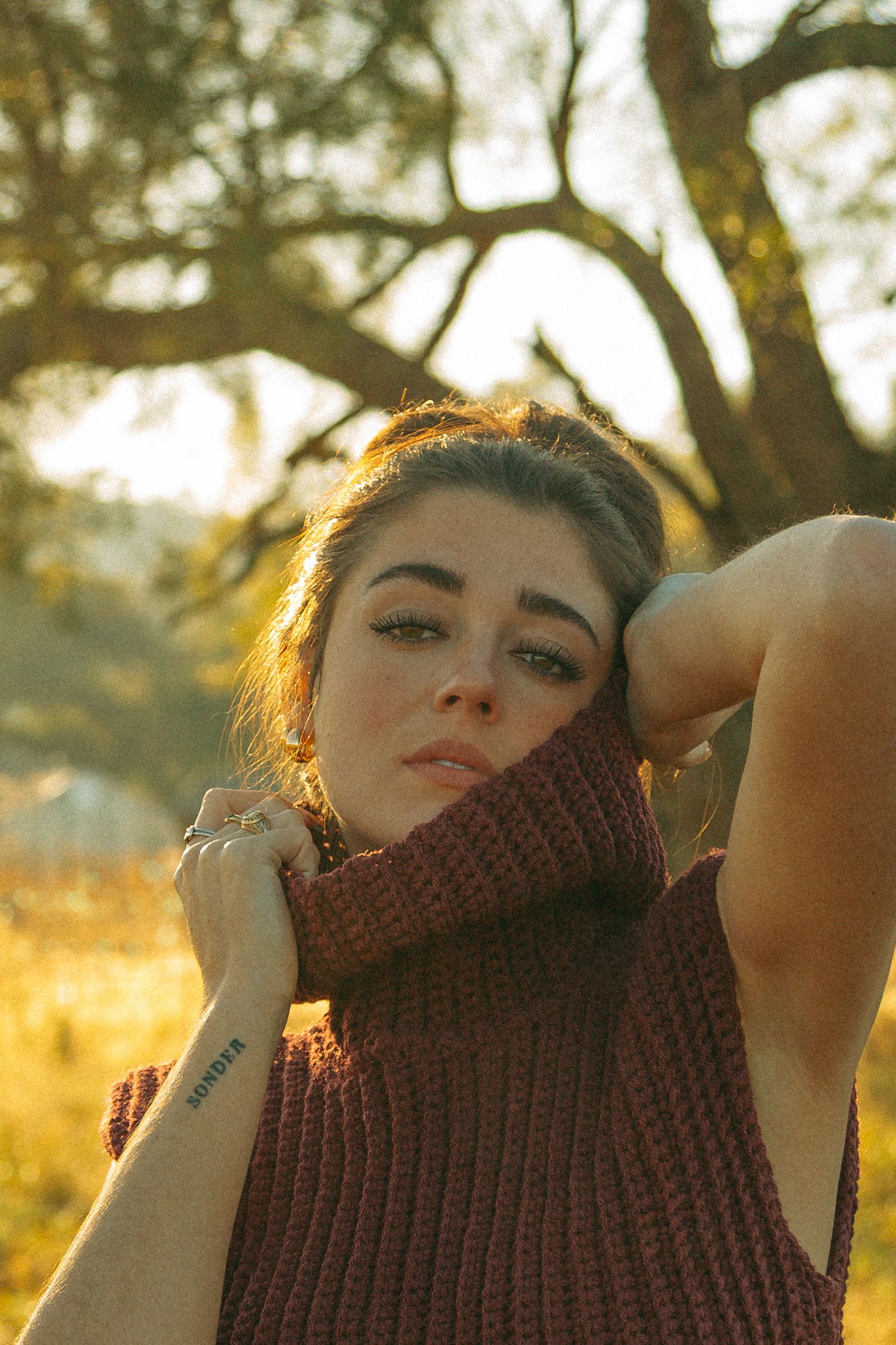 Close-up portrait with a brown knitted turtleneck against a warm sunset background.