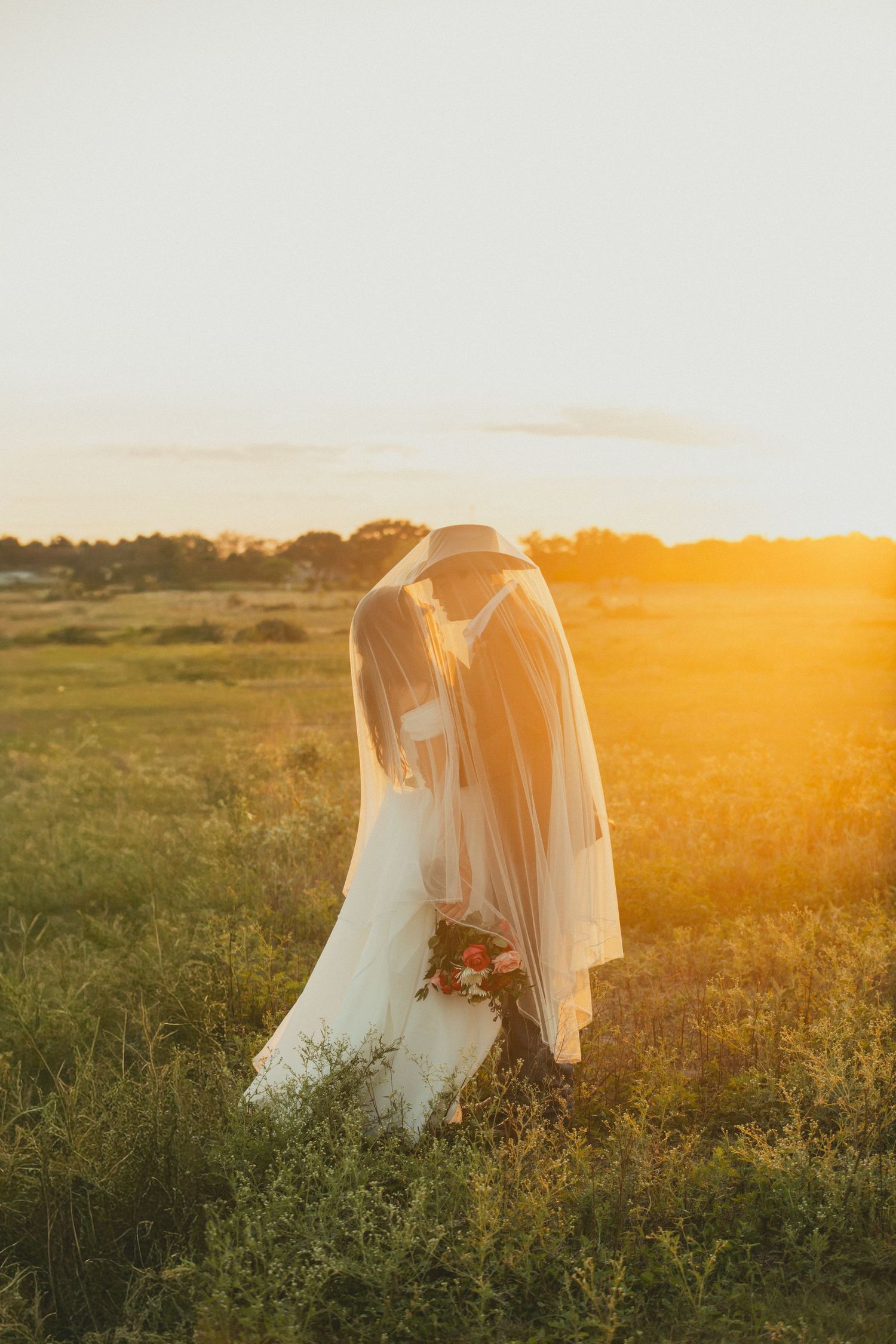 Wedding dresses glowing in warm sunset light across a grassy meadow.