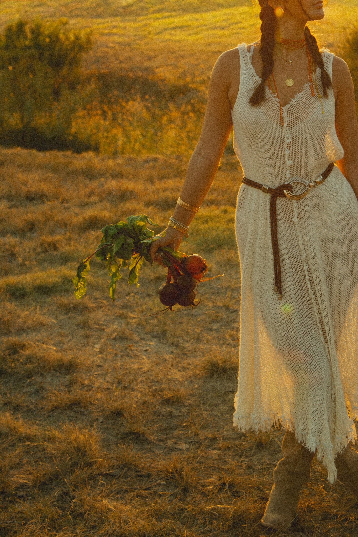 Woman in white dress walking through golden field at dusk.