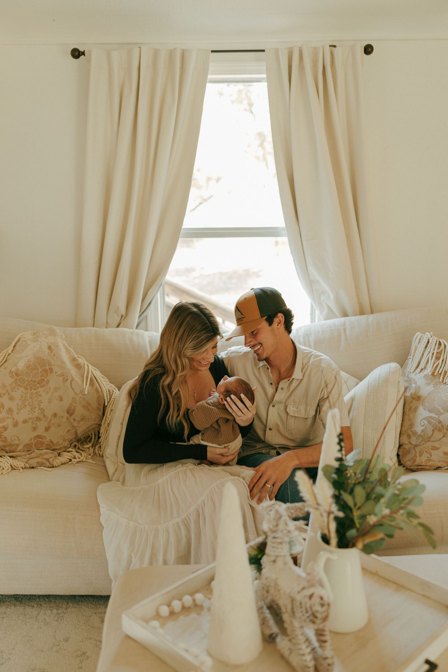 An intimate moment shared between and couple and their newborn on a white sofa in a sunlit room.
