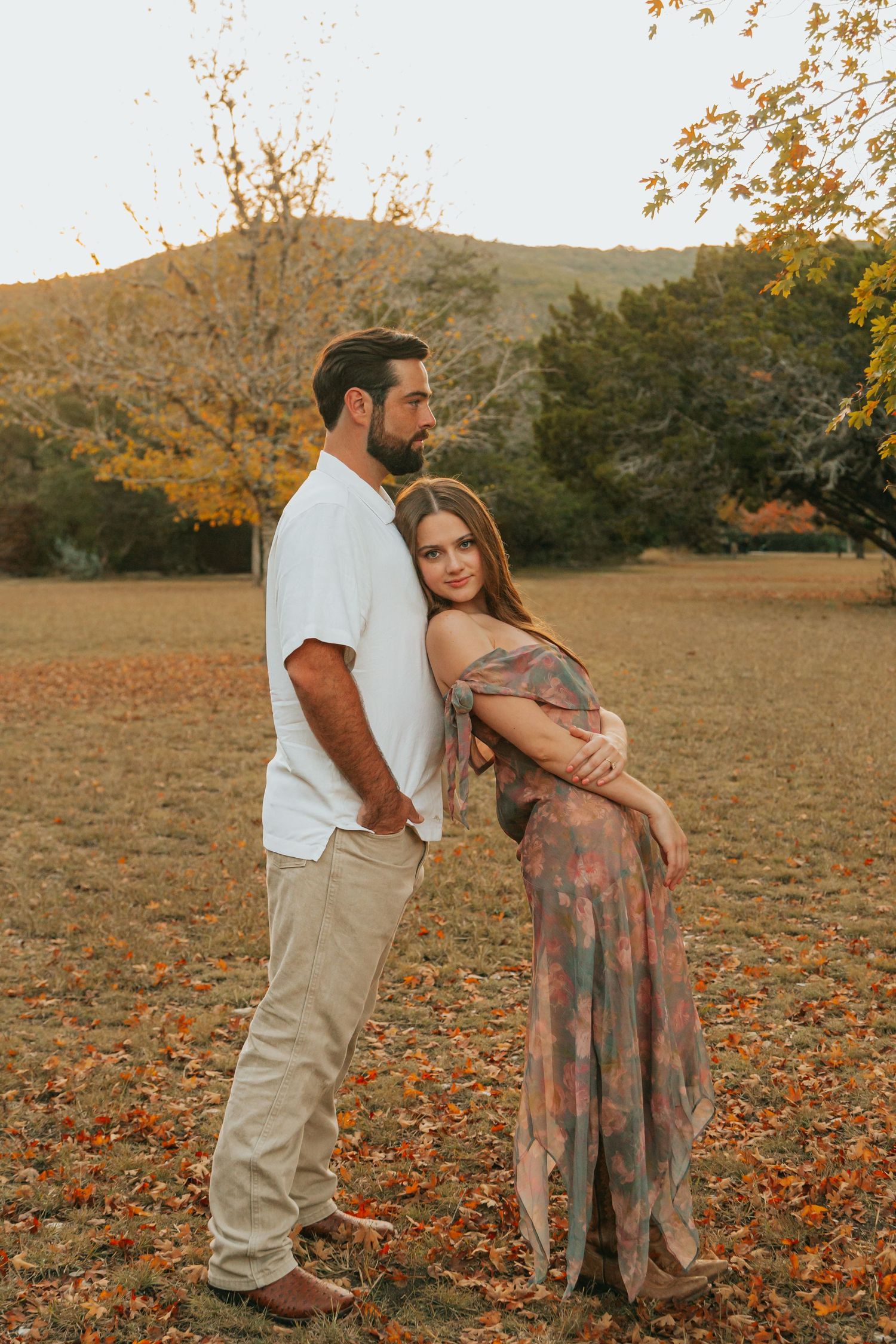 Romantic autumn engagement photo session in a field with fallen leaves at sunset.