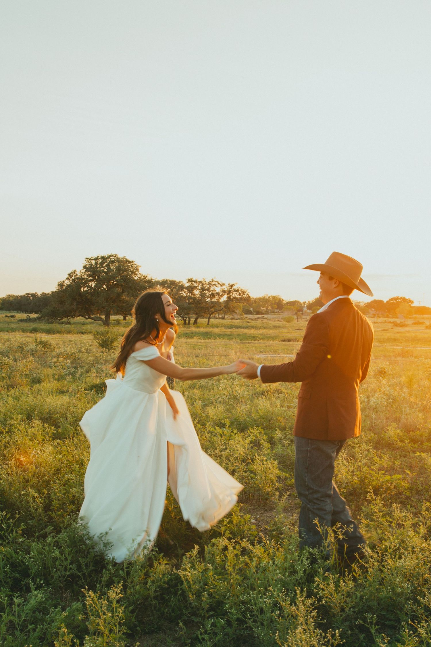 A joyful sunset wedding photo of a couple dancing in a wildflower field.