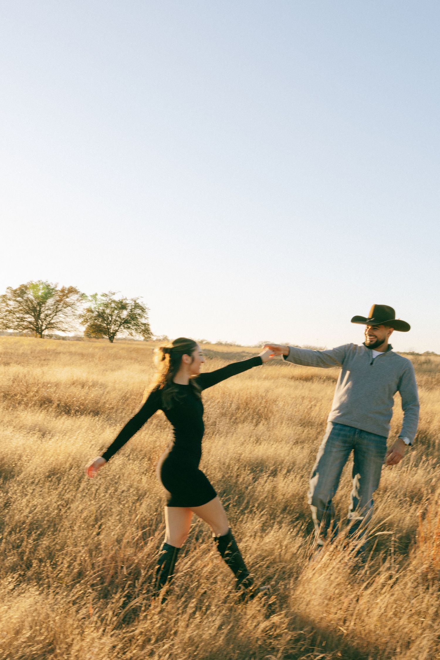 A couple striking playful poses in a sunlit golden field.