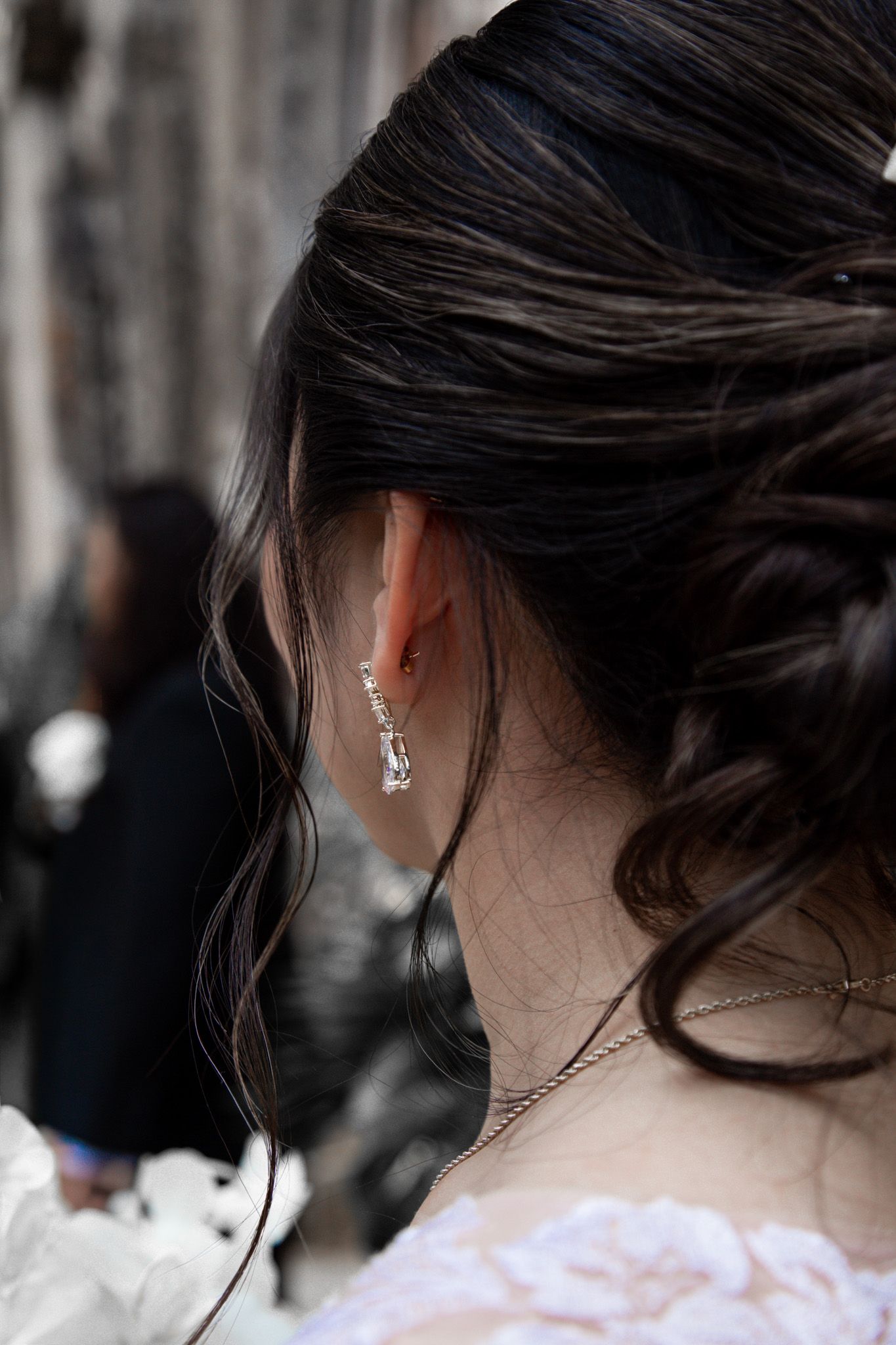 Close-up of bride's elegant updo hairstyle with sparkling drop earring and delicate necklace on wedding day.