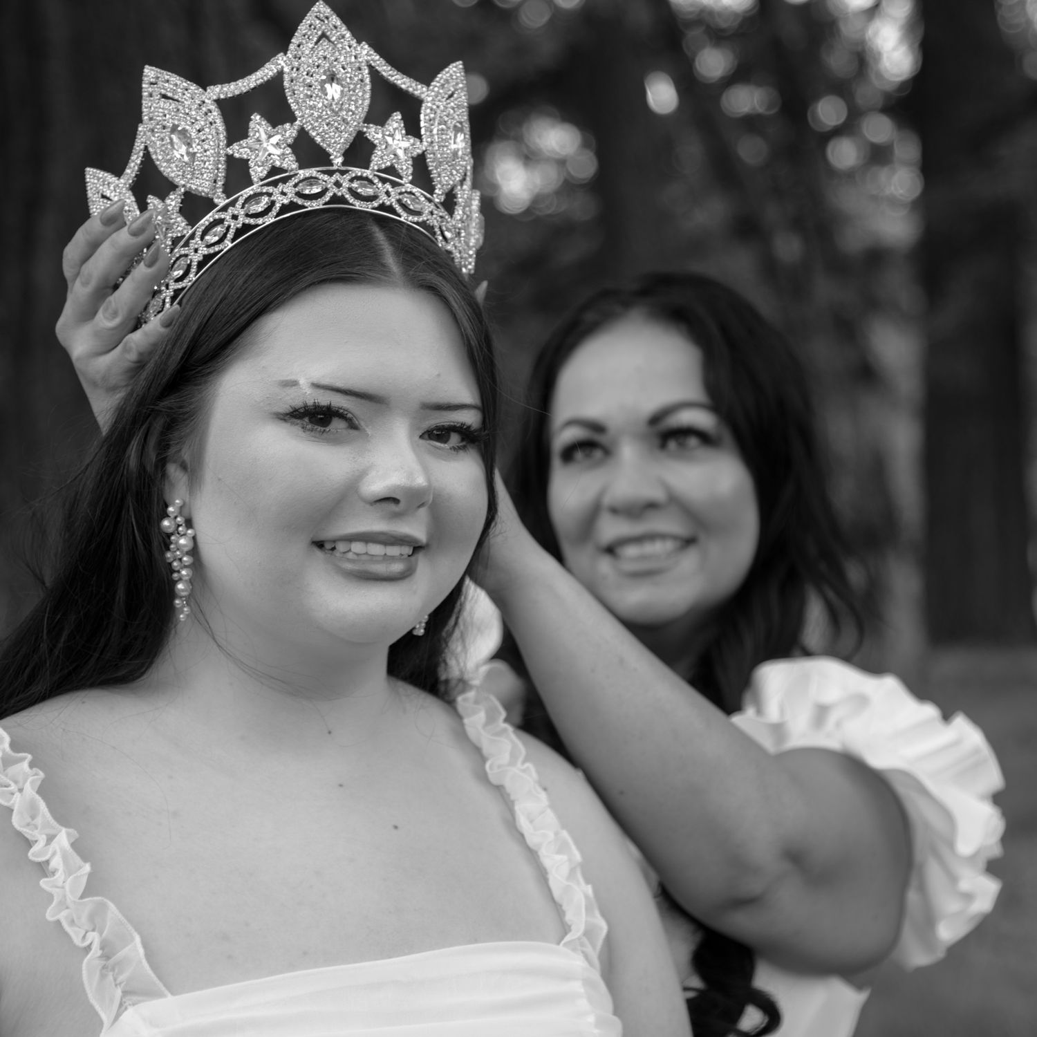 Black and white photo of a young woman being crowned with a tiara by another woman in formal attire.