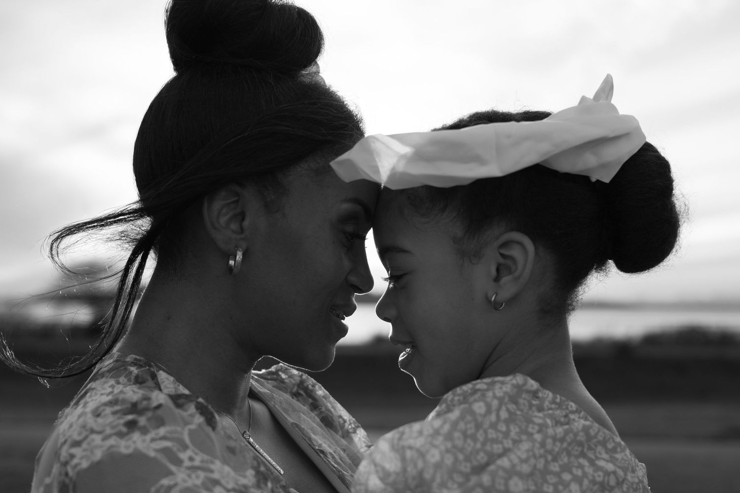 Black and white photo of two women touching foreheads in an intimate, tender moment outdoors.