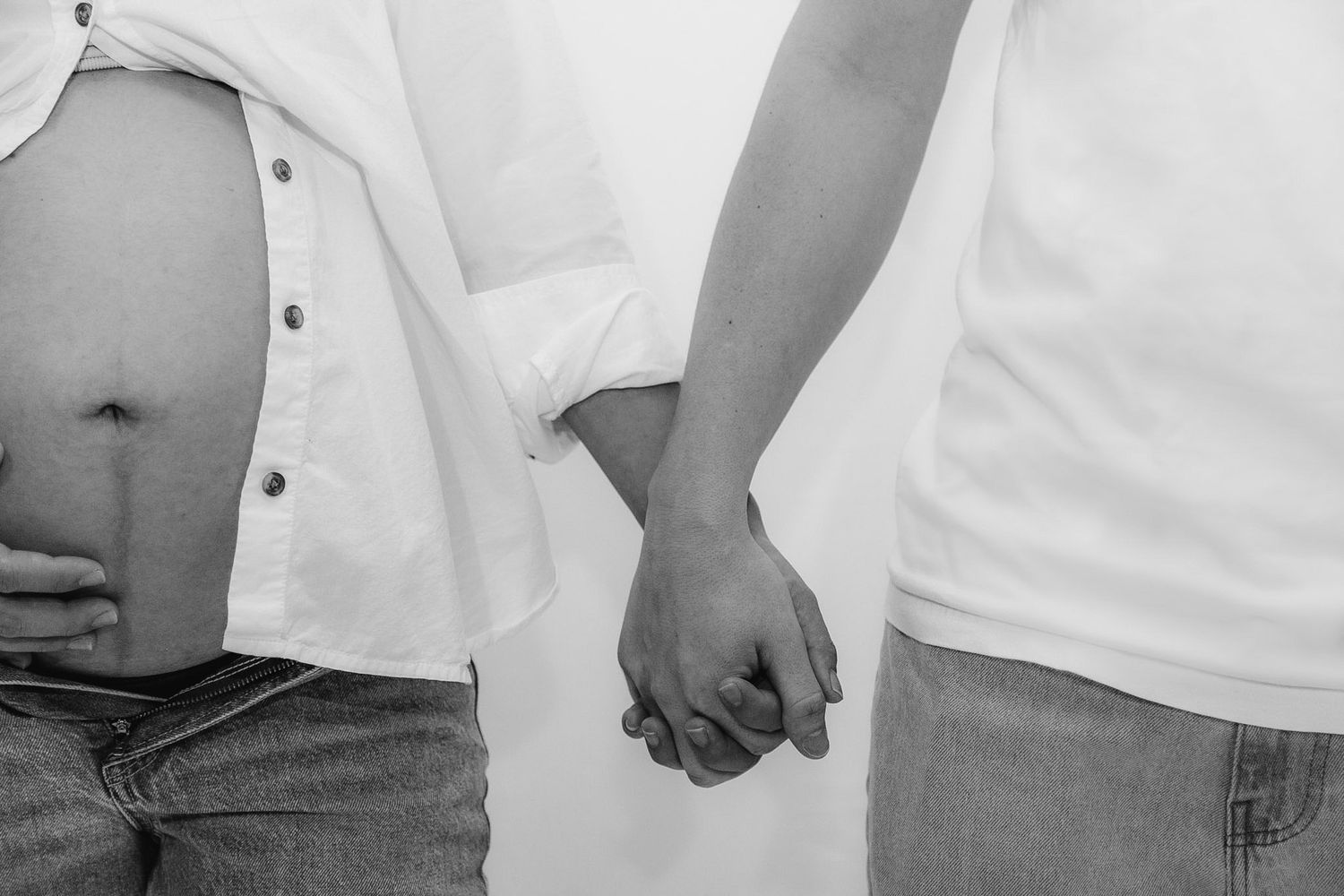 Black and white photo of pregnant couple holding hands showing baby bump in jeans.