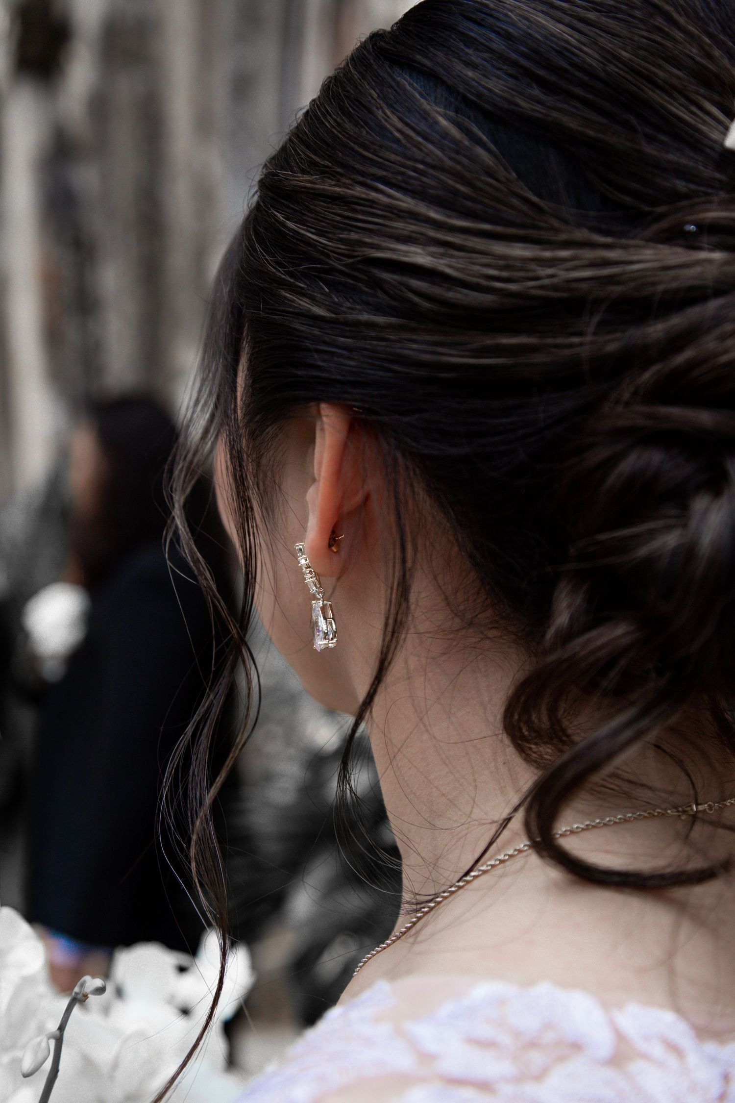 Close-up of a bride's elegant crystal drop earring with dark hair in an updo and delicate necklace.