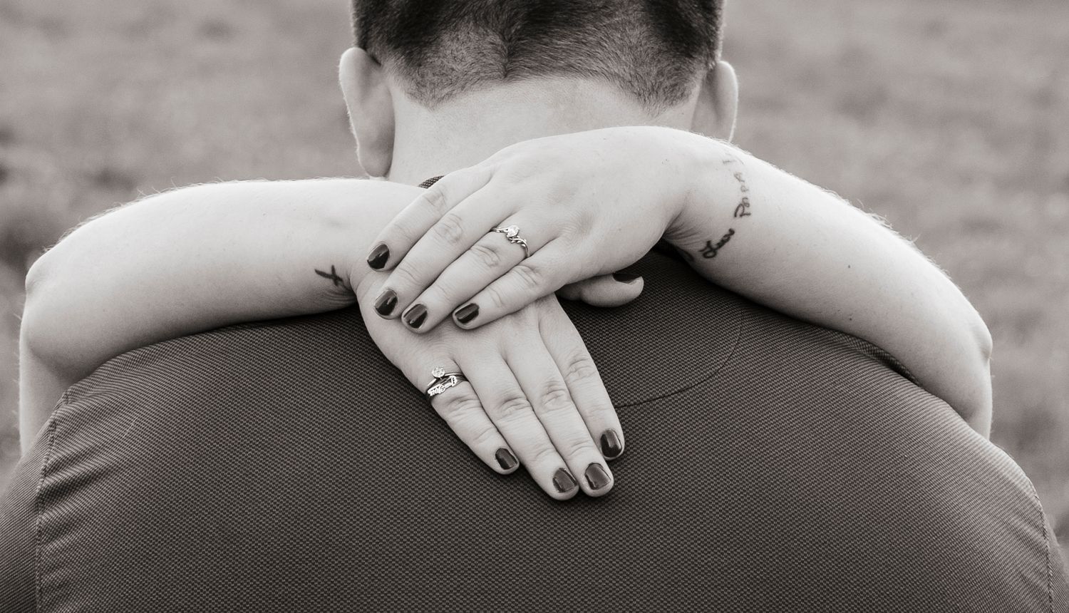 Black and white close-up of woman's hands with engagement ring wrapped around her partner's neck.