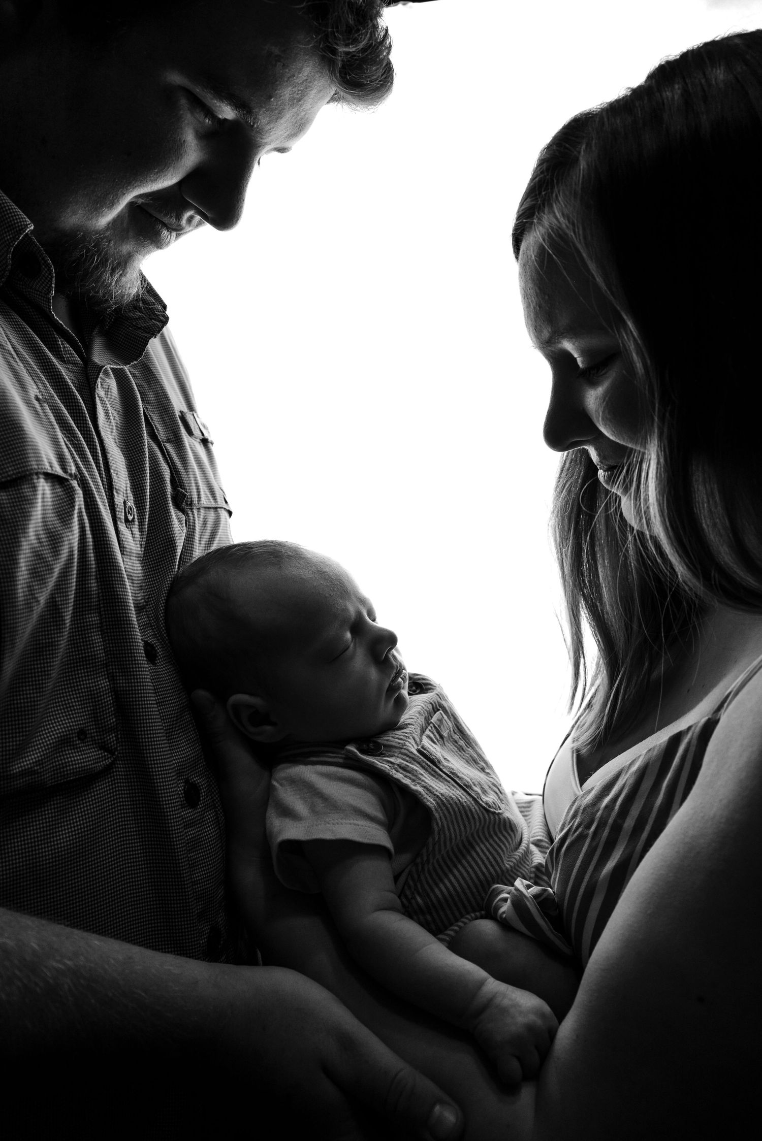 Black and white silhouette of parents lovingly gazing down at their newborn baby.