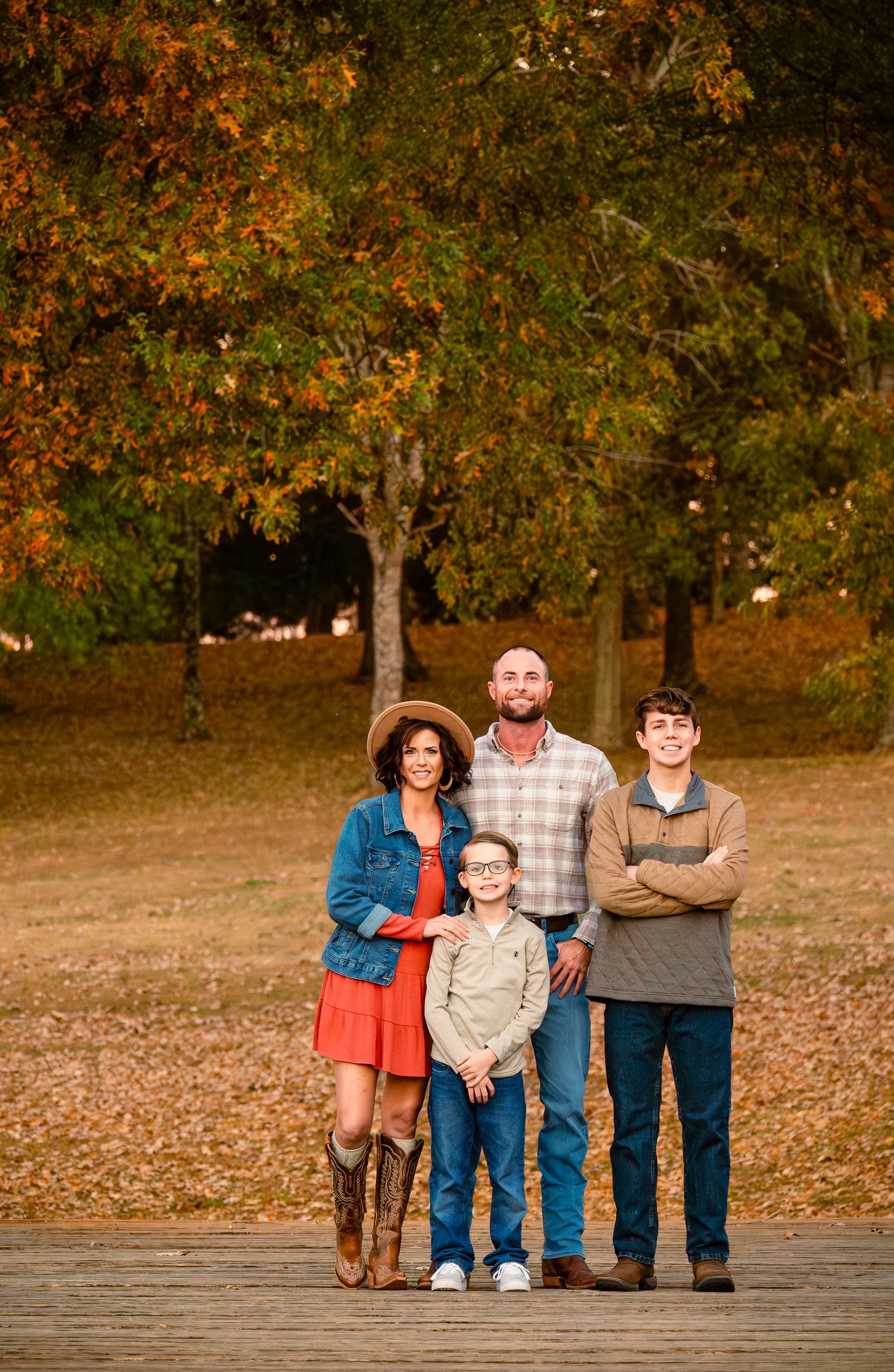 Family of four posing outdoors among autumn trees with colorful fall foliage in a warm seasonal portrait.