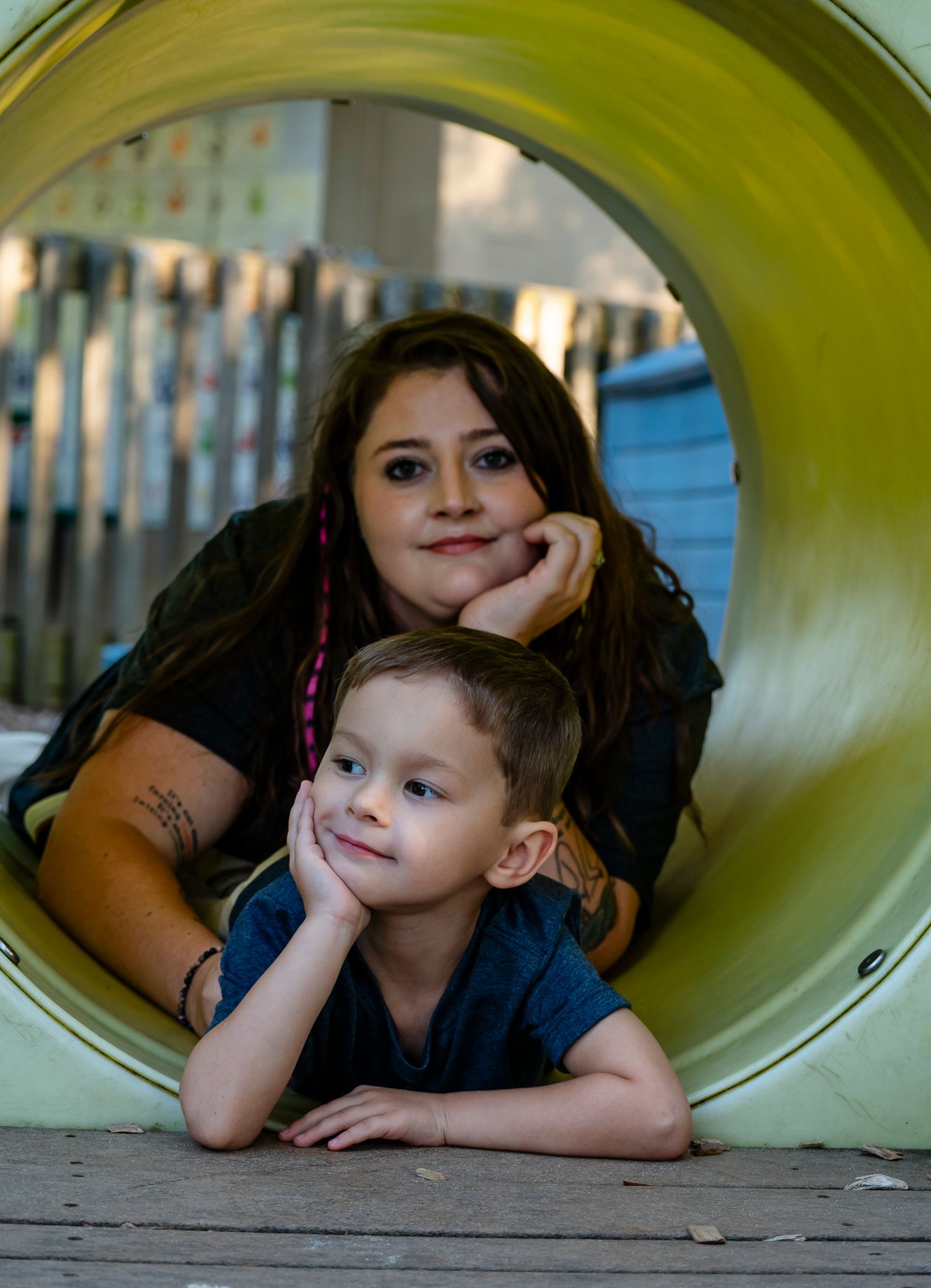 Woman and young boy posing together through a circular tunnel opening on a playground.