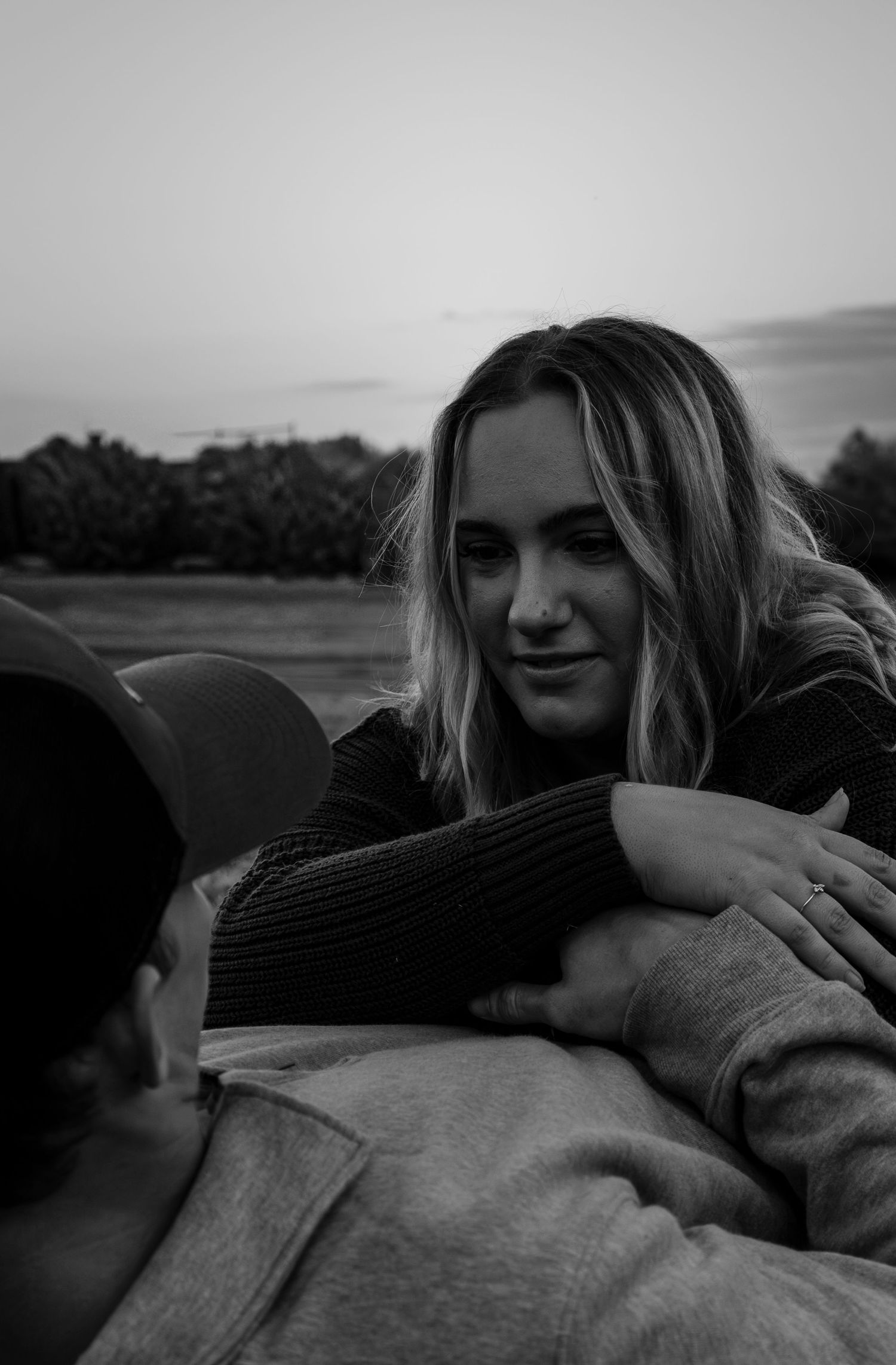 Black and white photo of smiling blonde woman leaning over her partner outdoors at dusk.