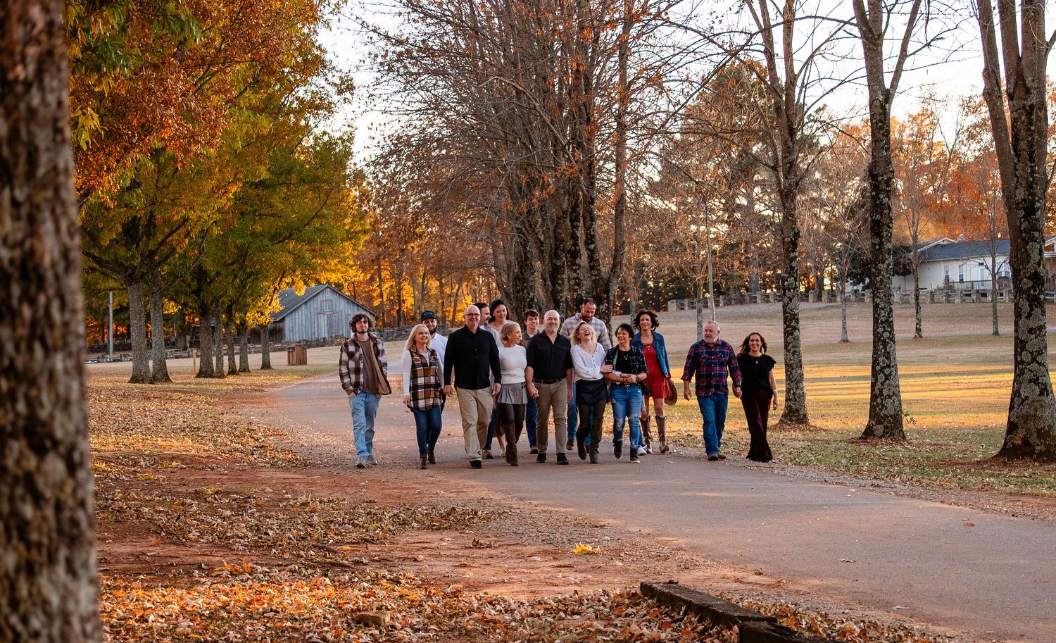 Large extended family walks together along a tree-lined path during a fall outdoor photo session.