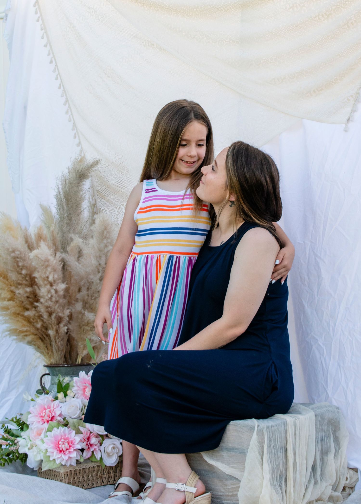 A tender moment as a mother in a navy dress leans in to kiss her young daughter in a colorful striped dress.