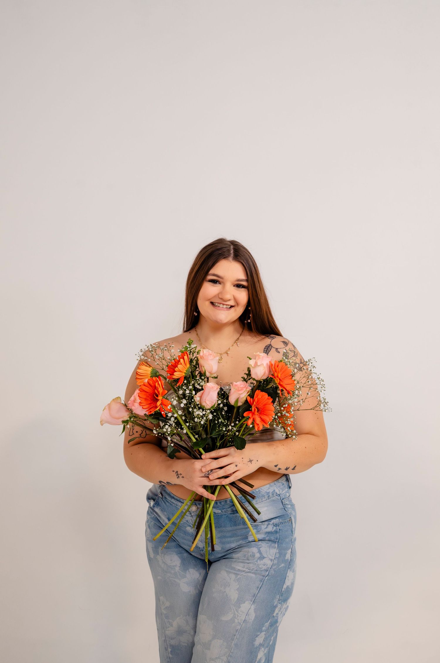 Smiling young woman holds a colorful bouquet of orange and pink roses in a bright studio setting.