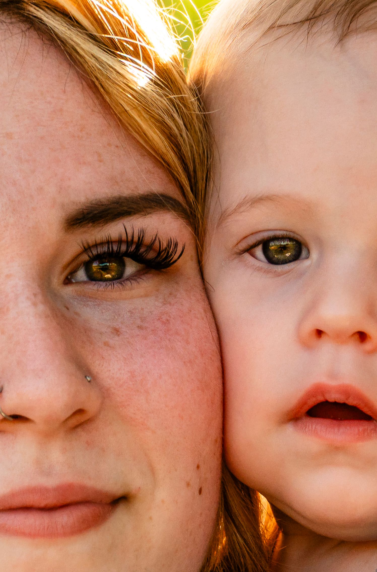 Close-up portrait of a freckled redhead woman and young toddler with matching green eyes cheek to cheek.