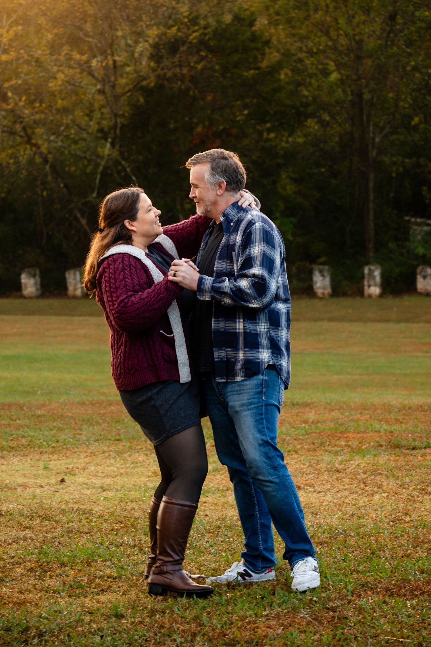 Couple dancing together in an autumn park, woman in burgundy sweater and man in plaid shirt, golden hour lighting.