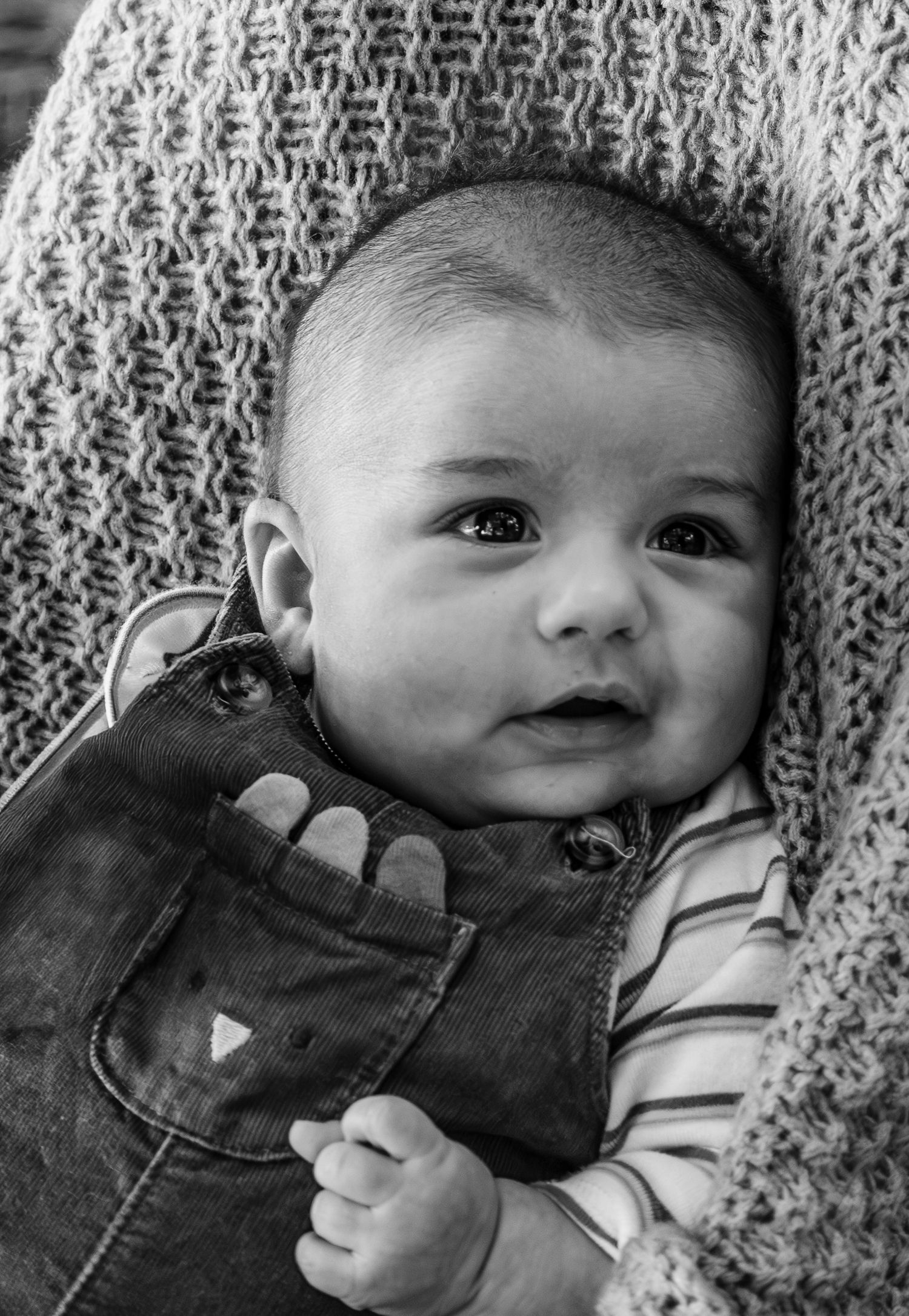 Black and white close-up portrait of an adorable baby in striped onesie and overalls.