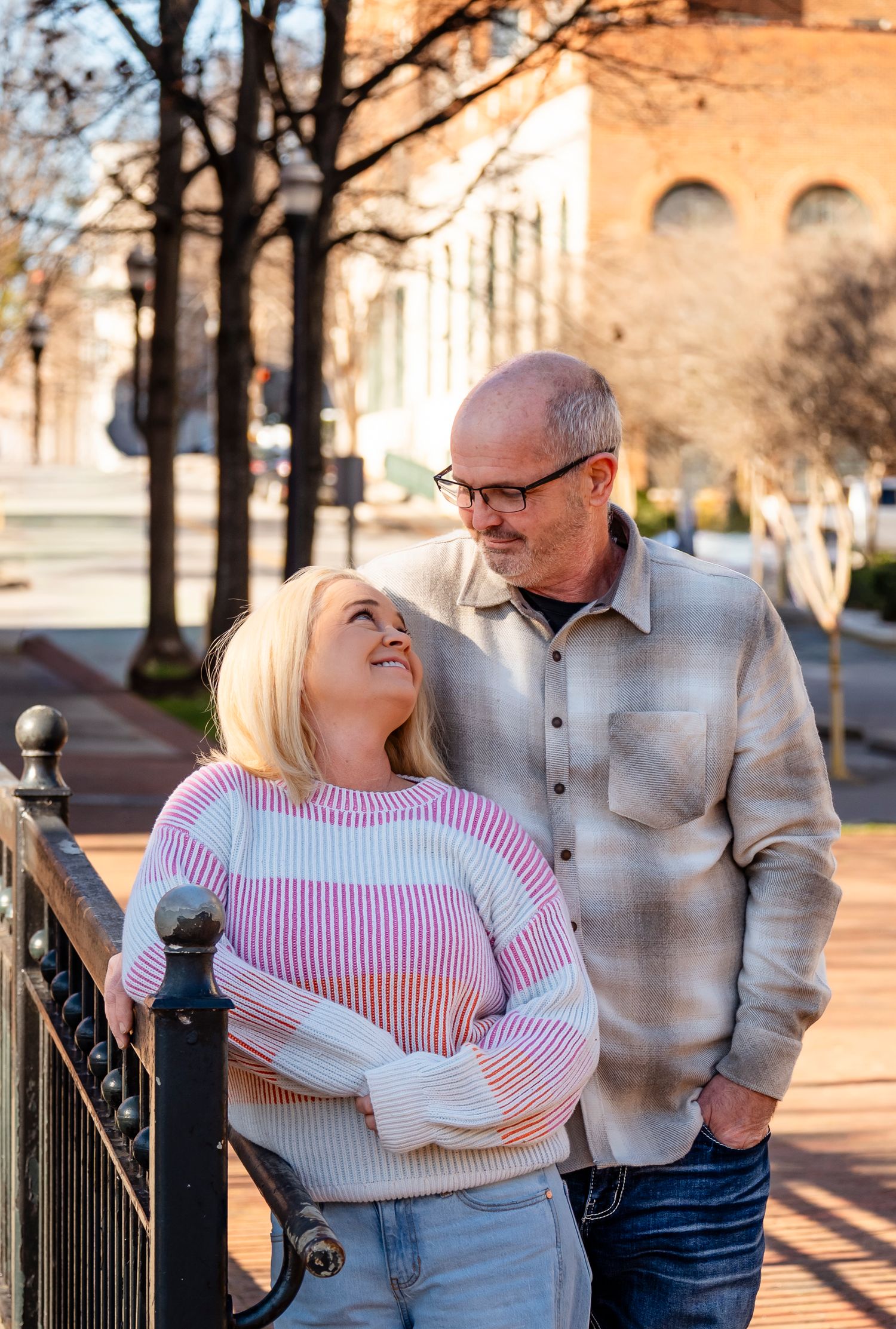 A smiling middle-aged couple sharing a warm moment outdoors on a city sidewalk near an iron railing.