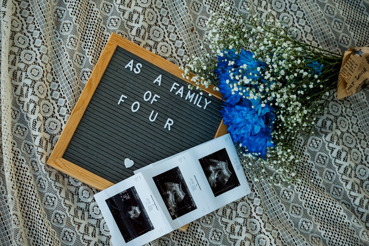 Letter board reading as a family of four with ultrasound photos and blue floral bouquet.