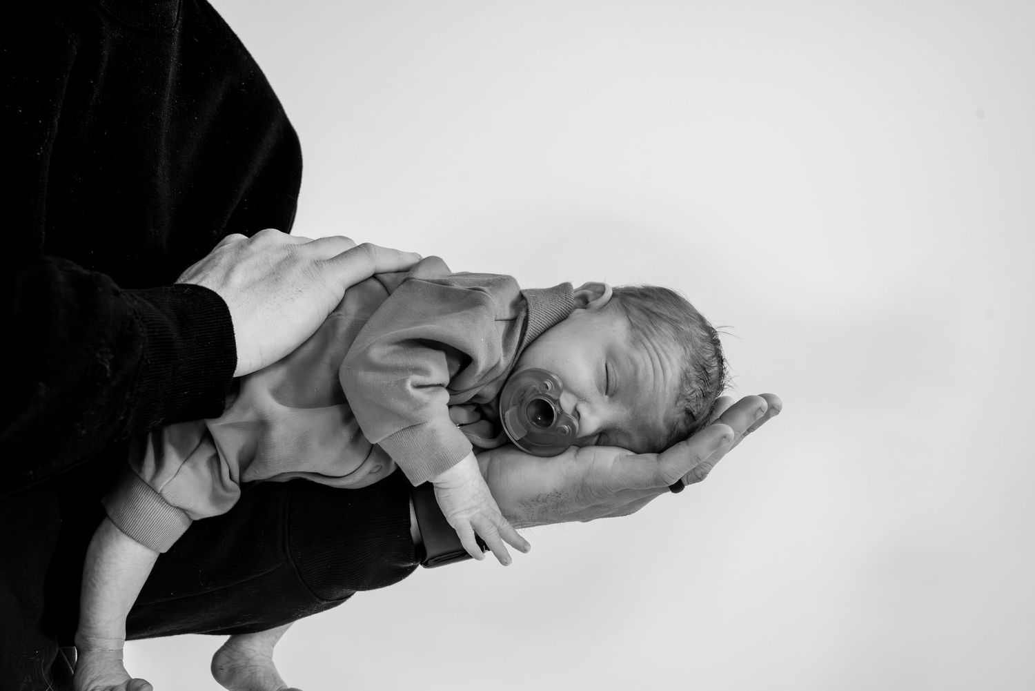Black and white photo of a newborn baby cradled in an adult's hands against a white background.
