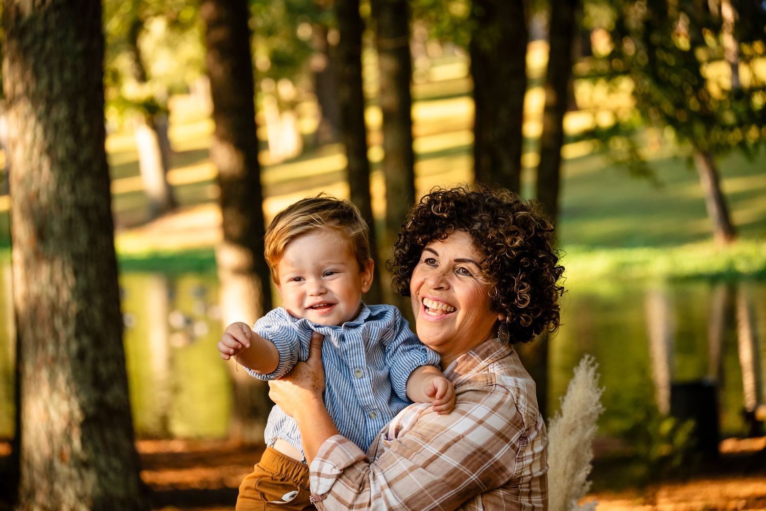 Curly-haired mother smiling while holding laughing toddler in sunny fall park.
