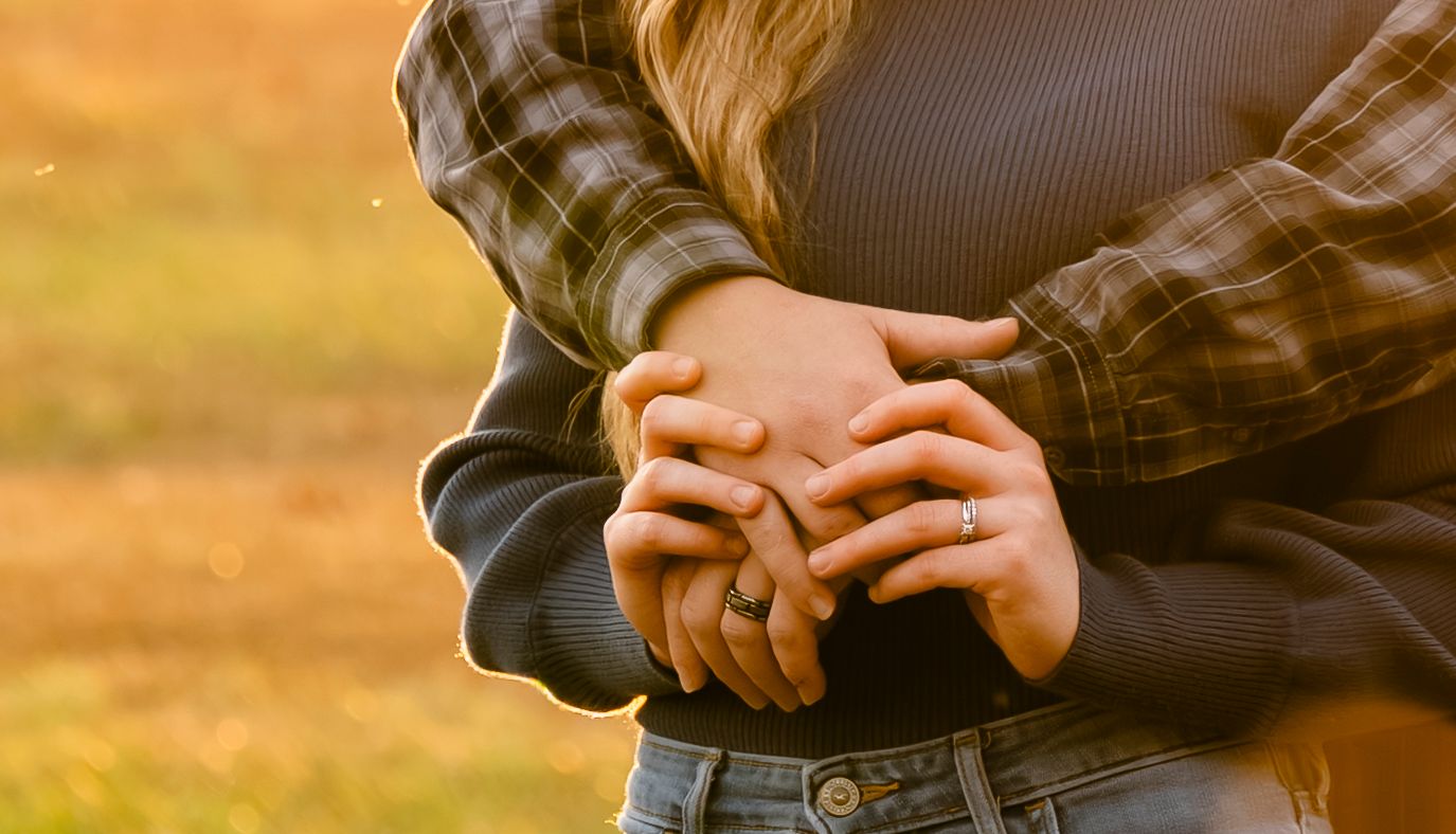 Couple embracing outdoors with hands intertwined, golden autumn bokeh background.