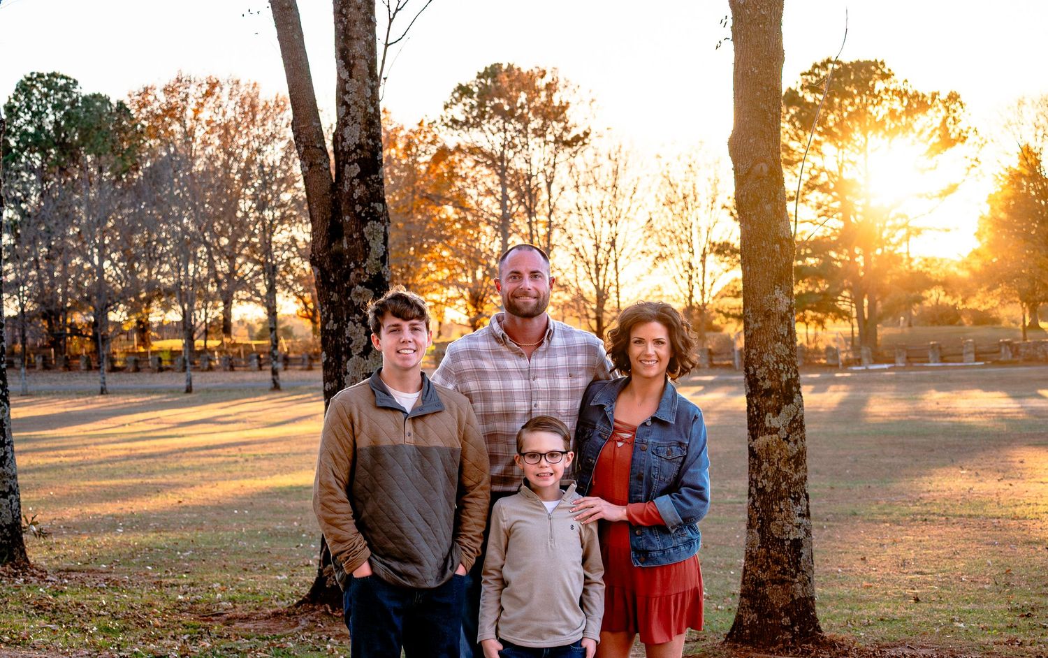 Family of four poses together at golden hour among autumn trees during an outdoor fall photo session.