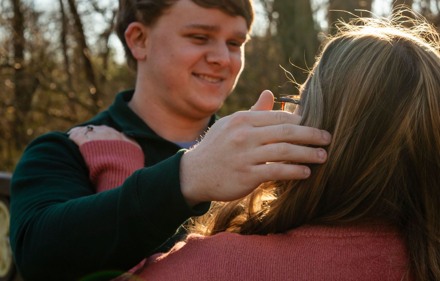 Young man tenderly touching a woman's hair in a warm golden outdoor setting.
