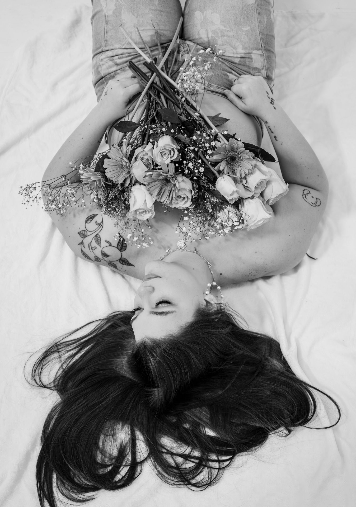 Black and white photo of woman lying down holding a bouquet of roses and baby's breath flowers.