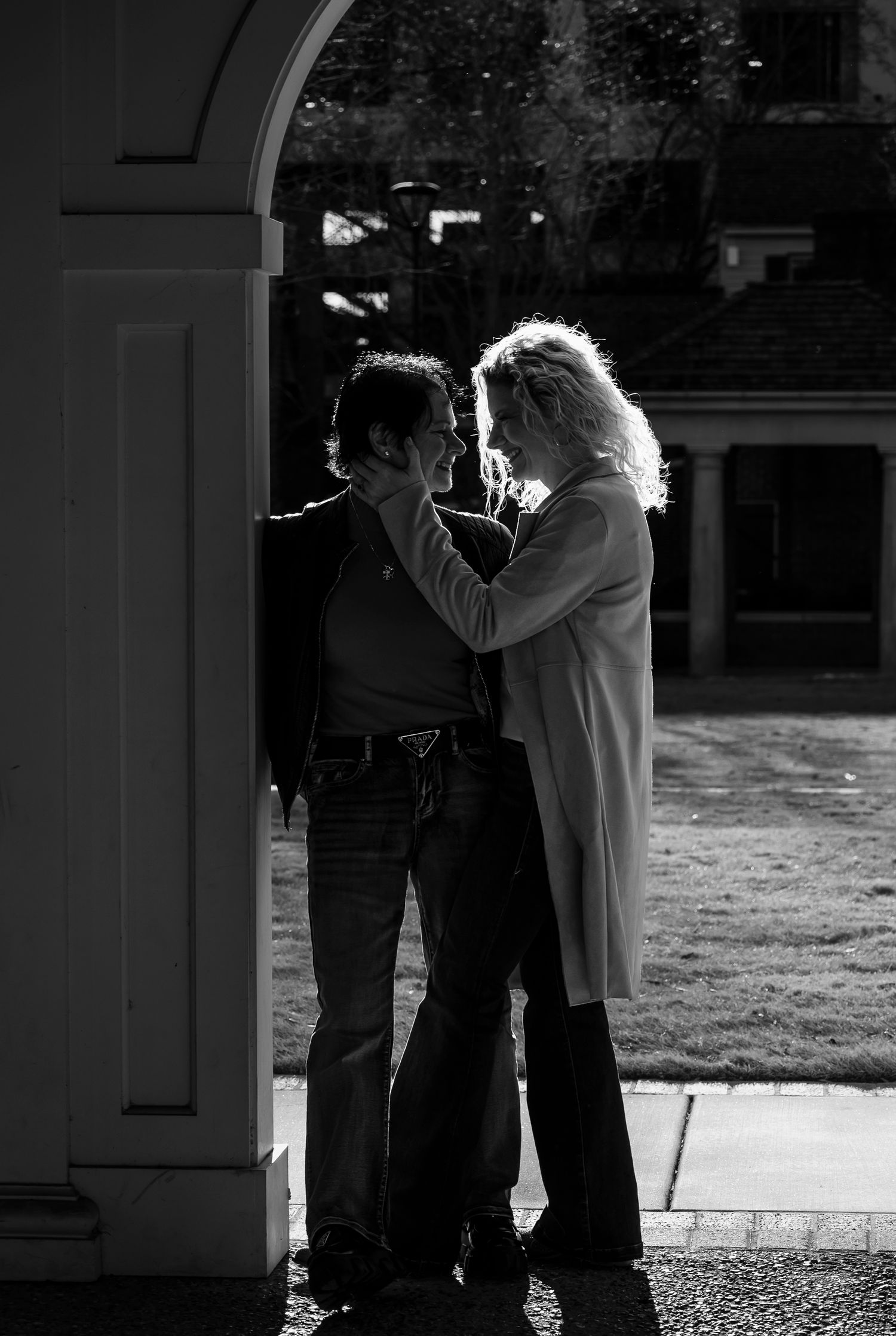 Couple standing close together under an archway in dramatic black and white light and shadow.