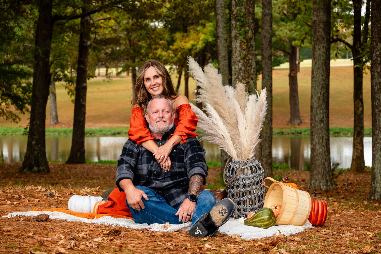 Couple posing with pumpkins and pampas grass vase in autumn park setting.
